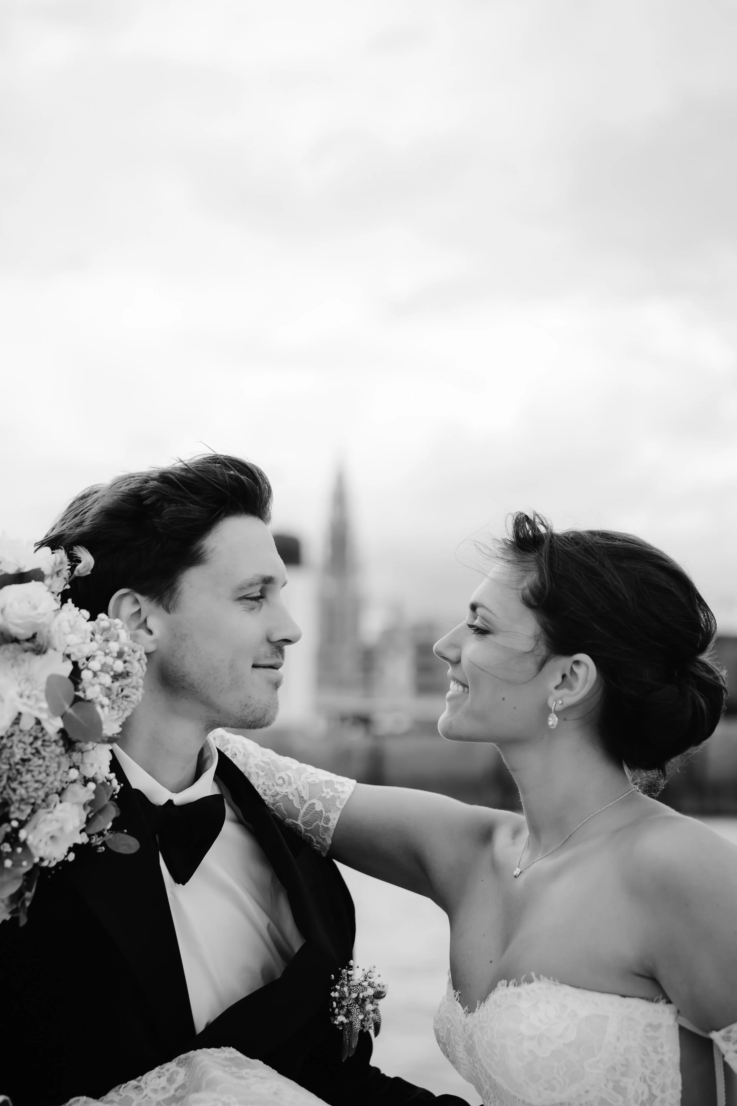 Bruid en bruidegom die naar elkaar lachen, met een stad op de achtergrond, zwart-wit foto.