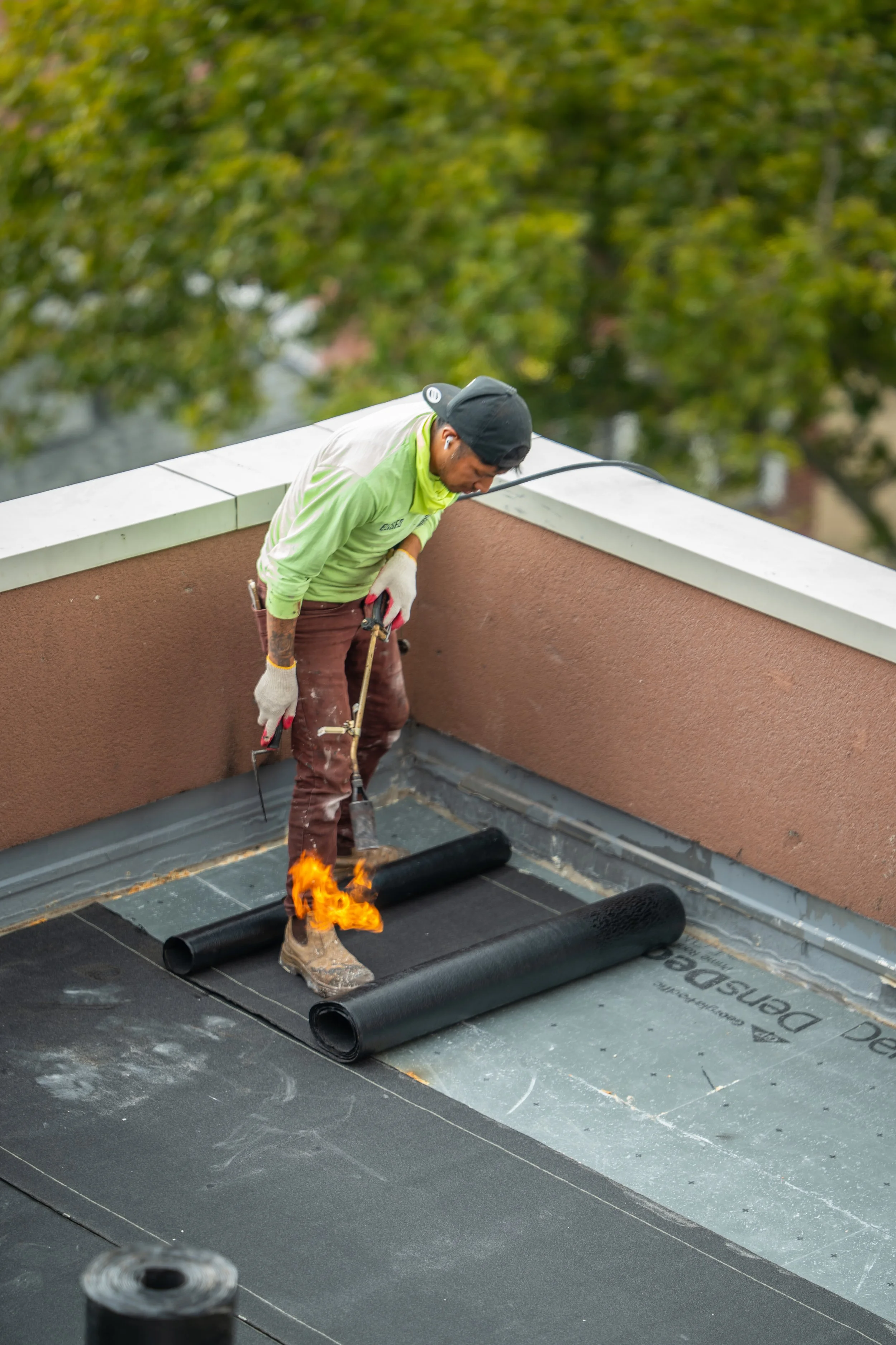 A worker on a flat rooftop installing roofing material with a torch.