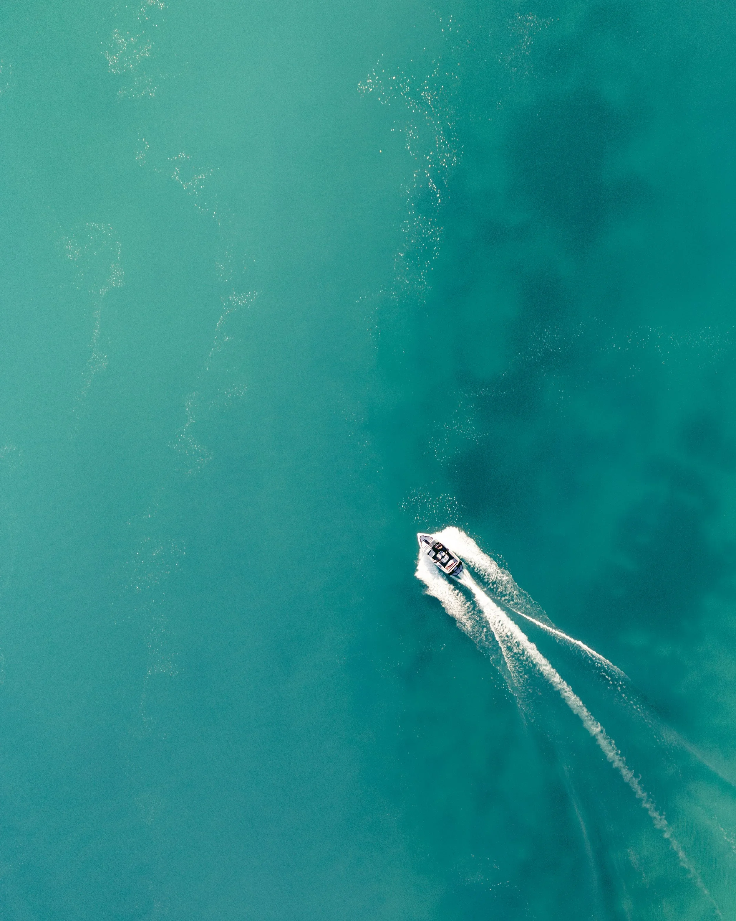 An aerial view of a large white yacht moving through the turquoise ocean, creating a trail of white foam behind it. Twizel Ohau Canal Lake River Fishing Salmon Trout. Stay at Lake Ohau Escape AirBnb Accomodation.