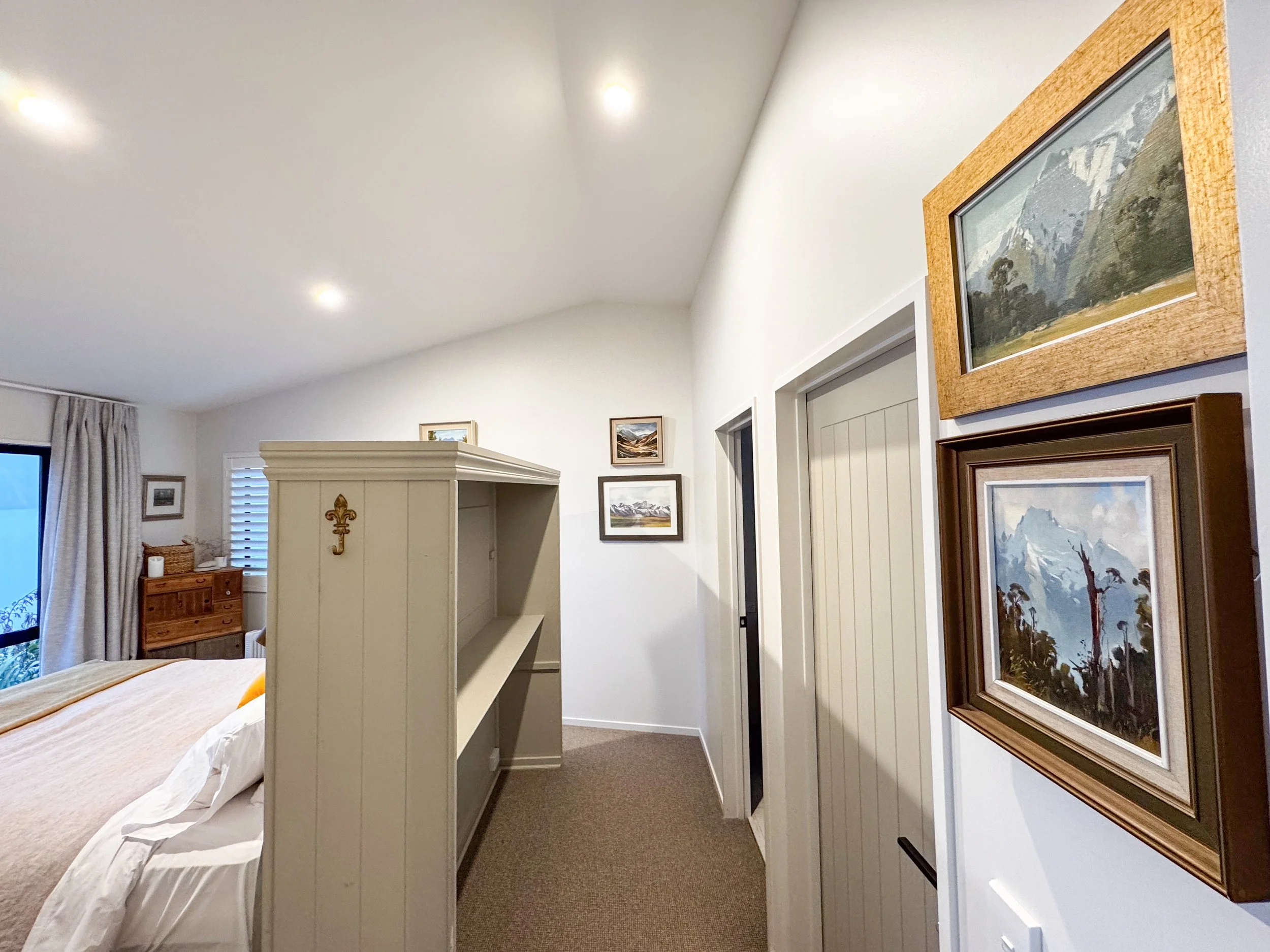 Part of a bedroom showing a framed landscape painting on a white wall and a ceiling with recessed lighting.