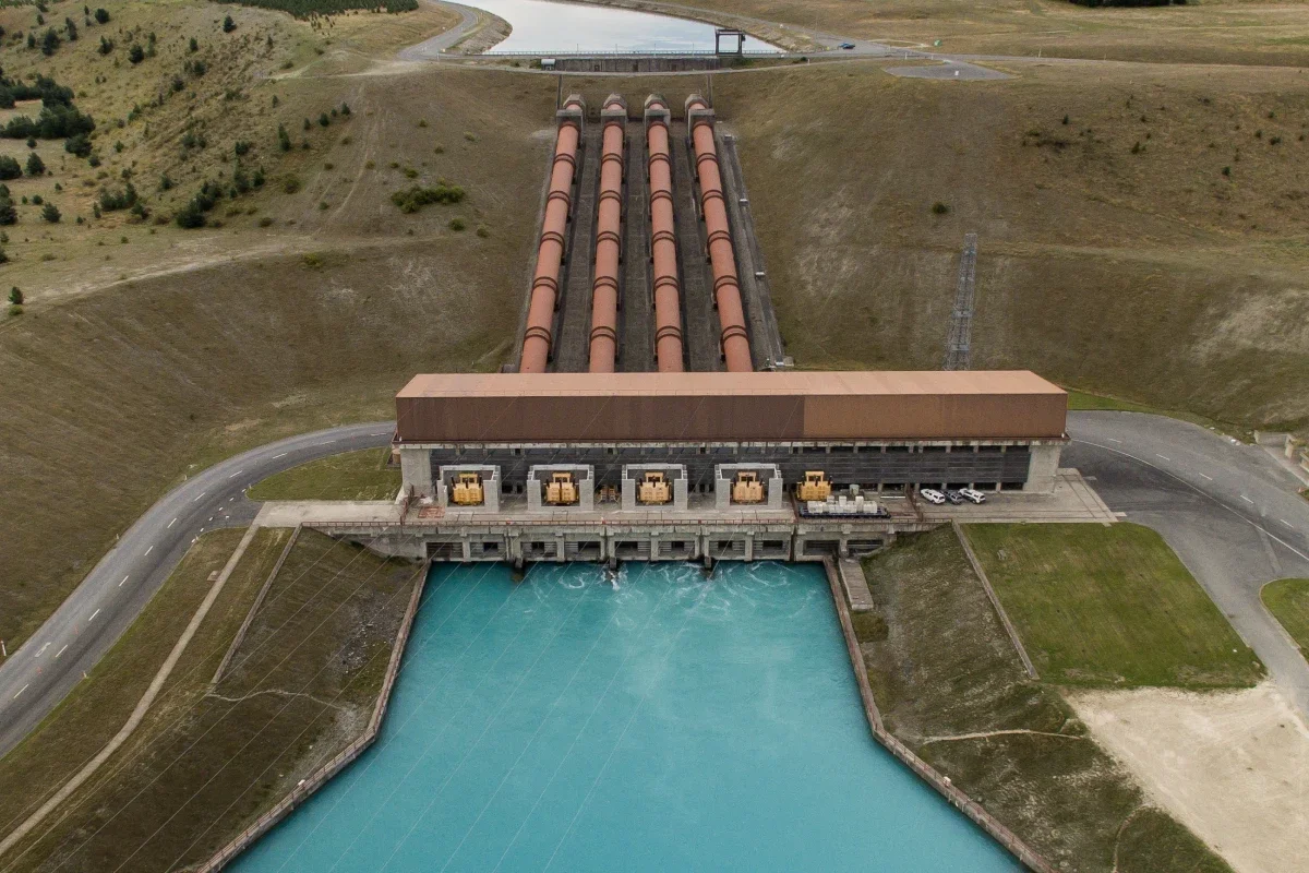 An aerial view of a hydroelectric dam with multiple large pipes releasing water into a reservoir.