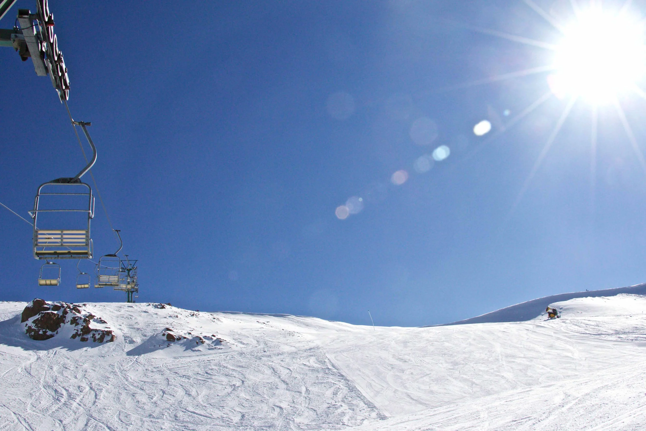 Ski lift chairs on a snowy mountain slope under a bright sun in a clear blue sky. Lake Ohau Ski Field