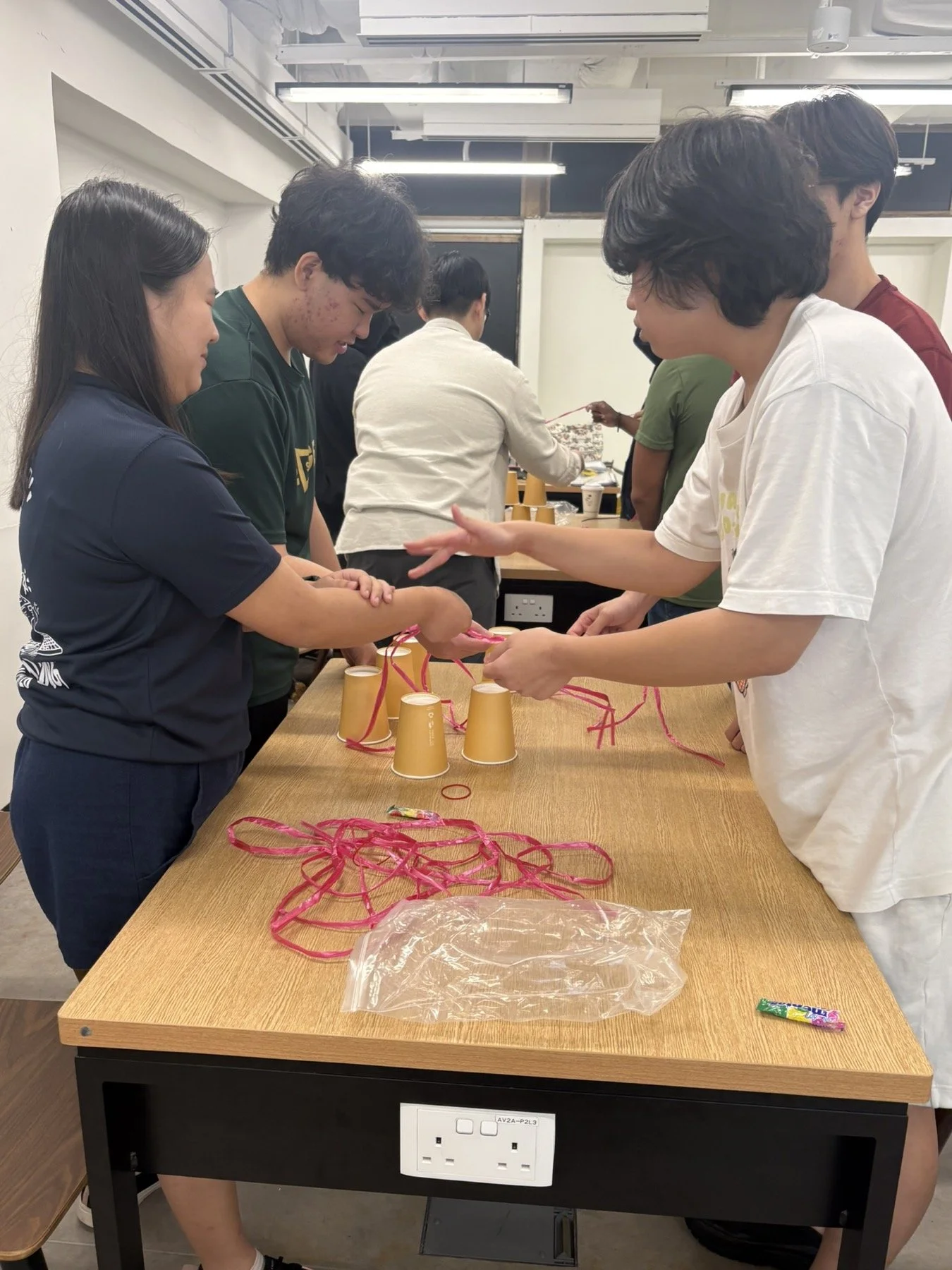 Polytechnic students stack cups with strings in a DISC teamwork challenge