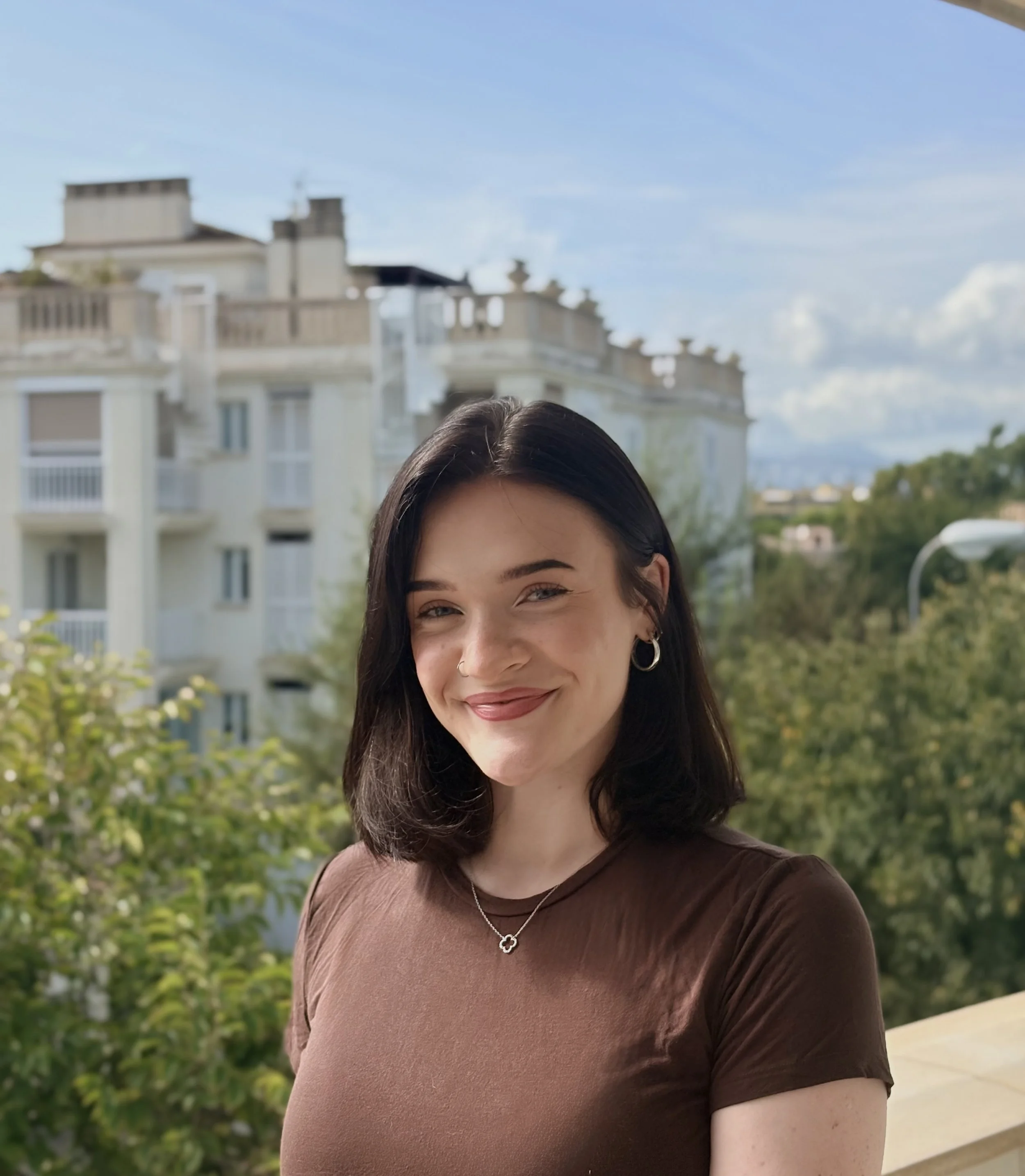 Woman with brown hair smiling standing in front of a building
