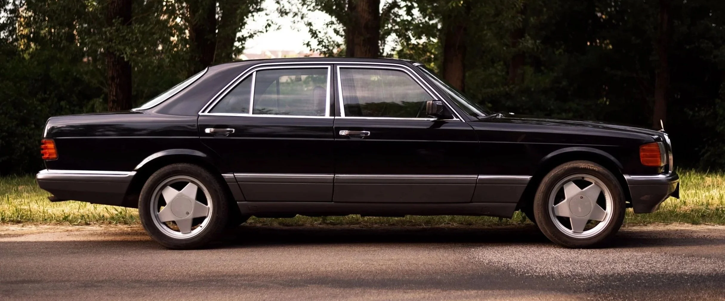 Side view of a black vintage luxury sedan parked on a road with trees in the background.