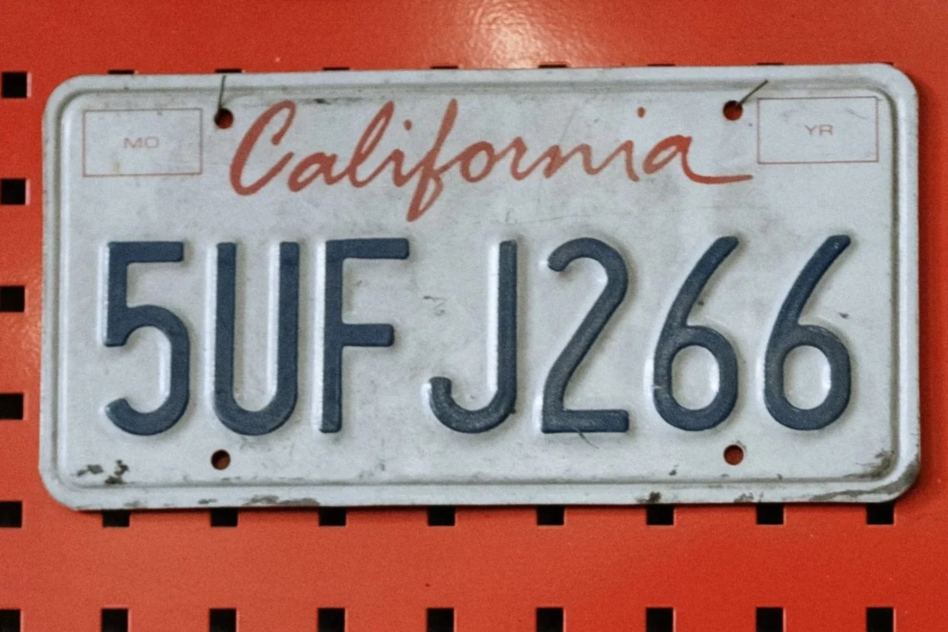 A vintage Californian license plate reading 'SUF J26G' with red 'California' text at the top, mounted on a red background.
