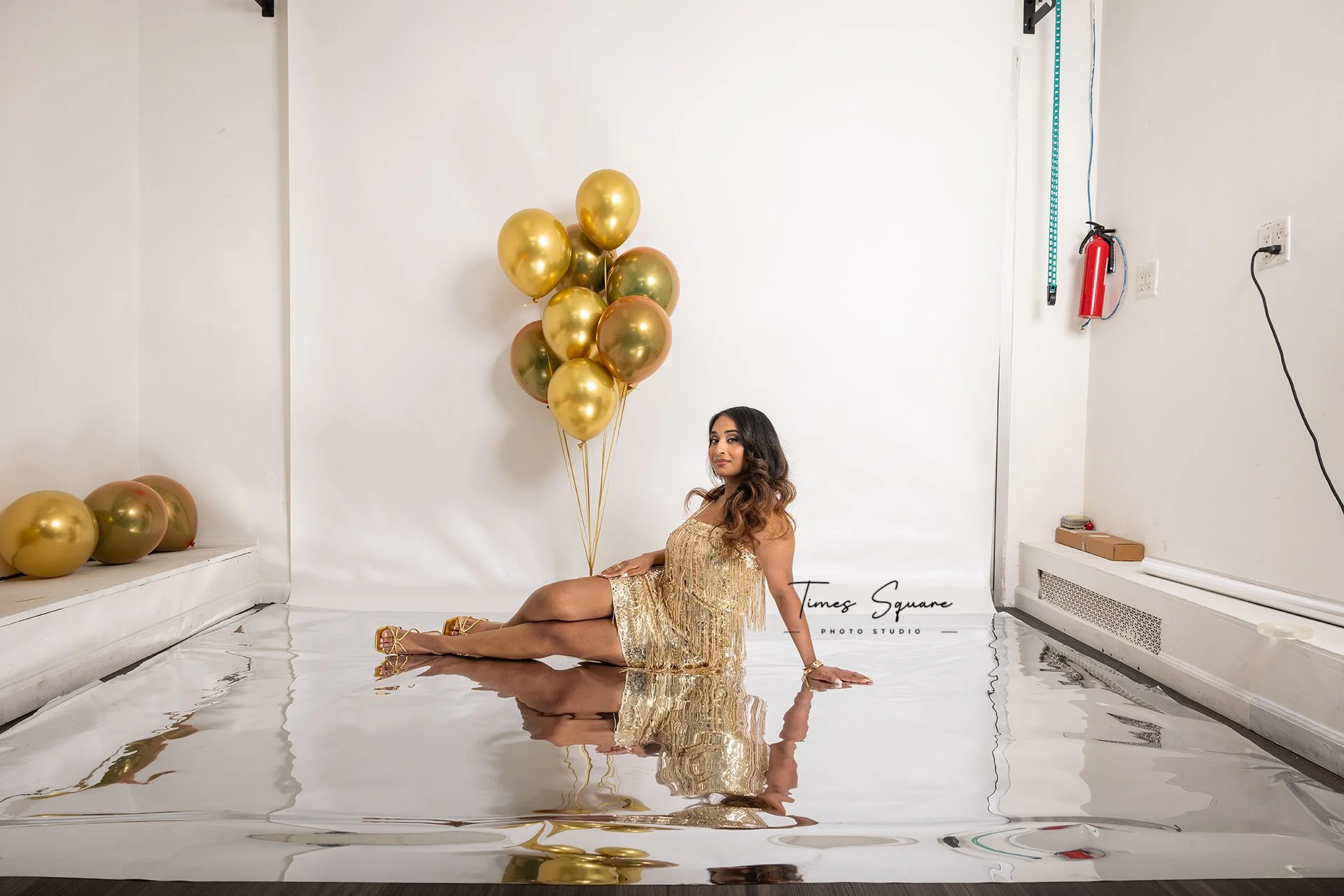 Behind-the-scenes studio view of a birthday photoshoot setup with gold balloons and reflective flooring, highlighting the creative studio environment.