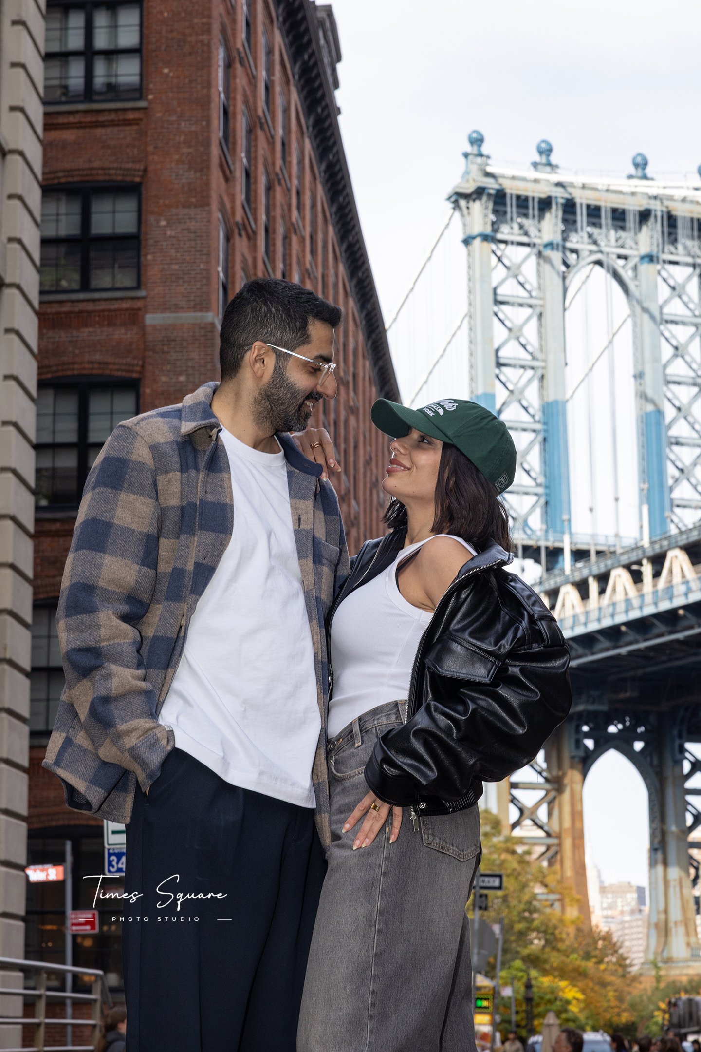 a couple posing in DUMBO in front of Manhattan bridge for a love story vacation photoshoot in Brooklyn New York