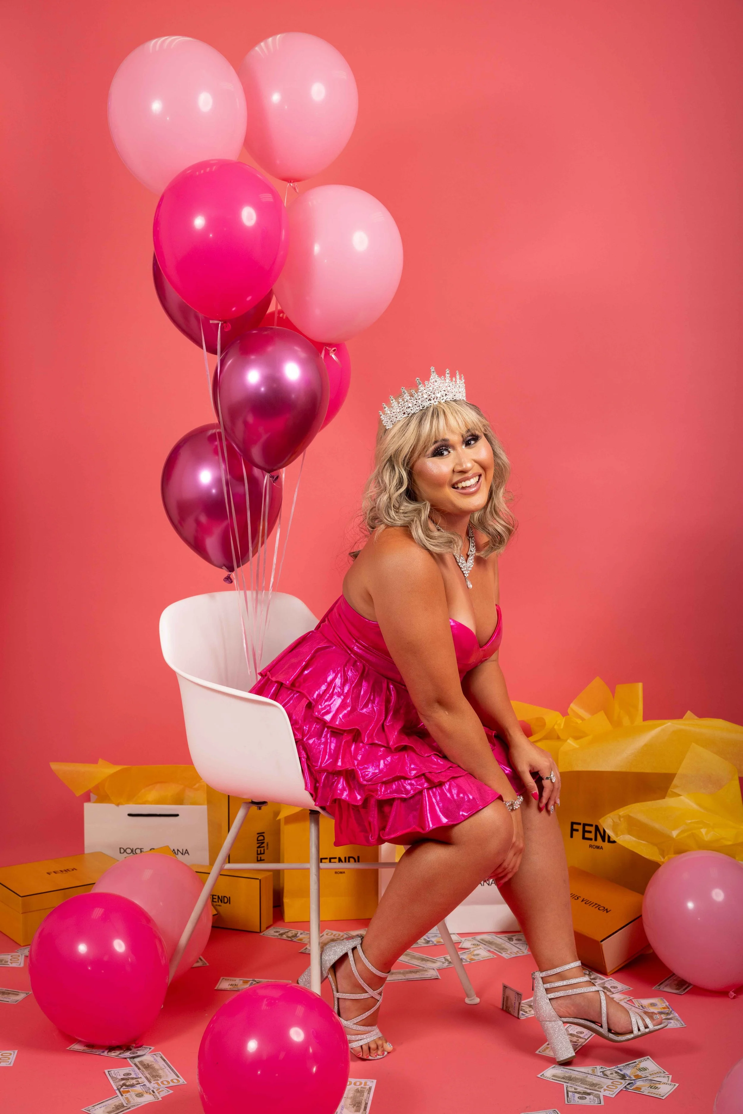 a woman posing for her birthday studio photoshoot in New York City. All pink birthday decor, with pink balloons, luxury designer shopping bags and money scattered on the floor