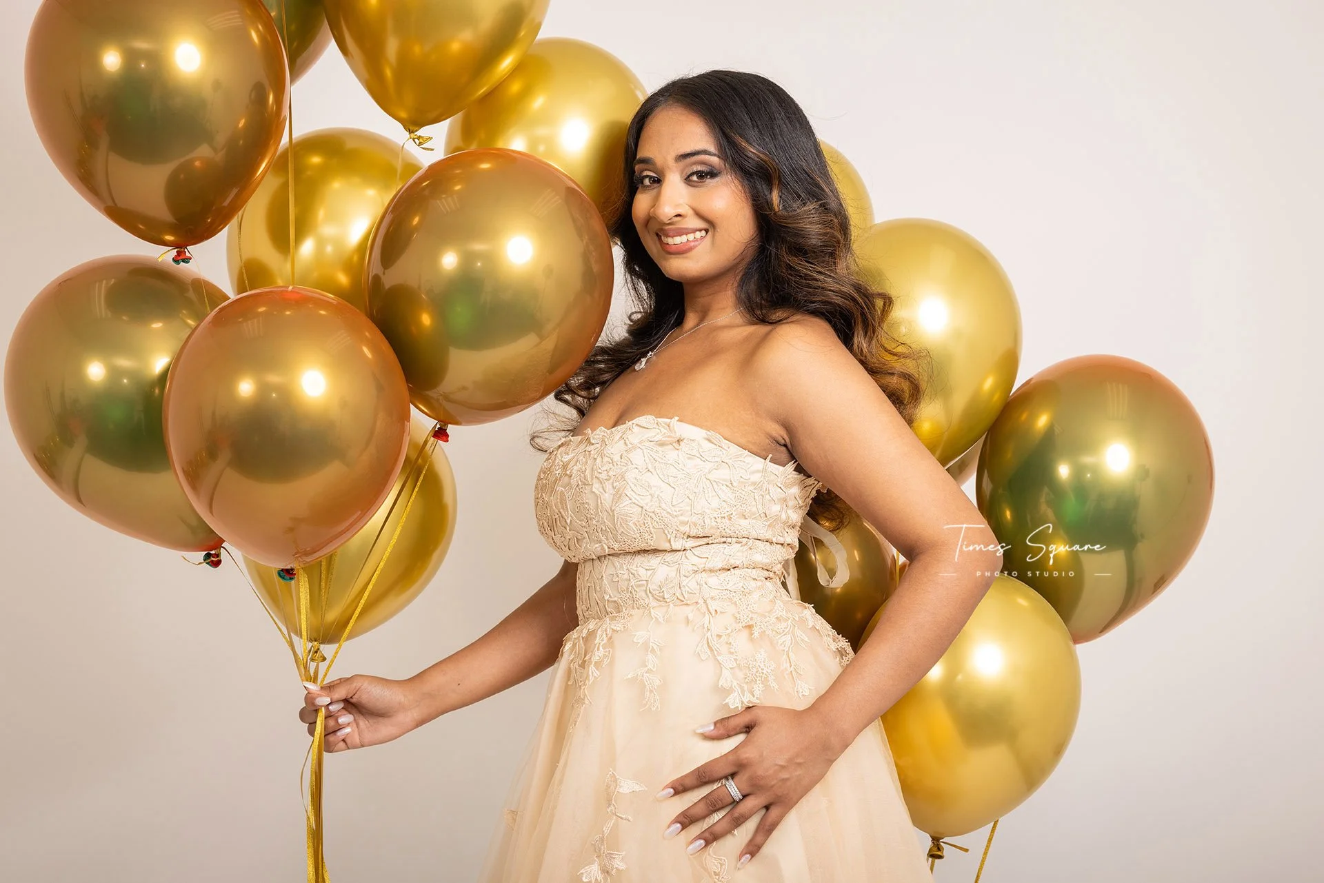 a woman holding a lot of gold balloons posing for her birthday studio photoshoot in New York City