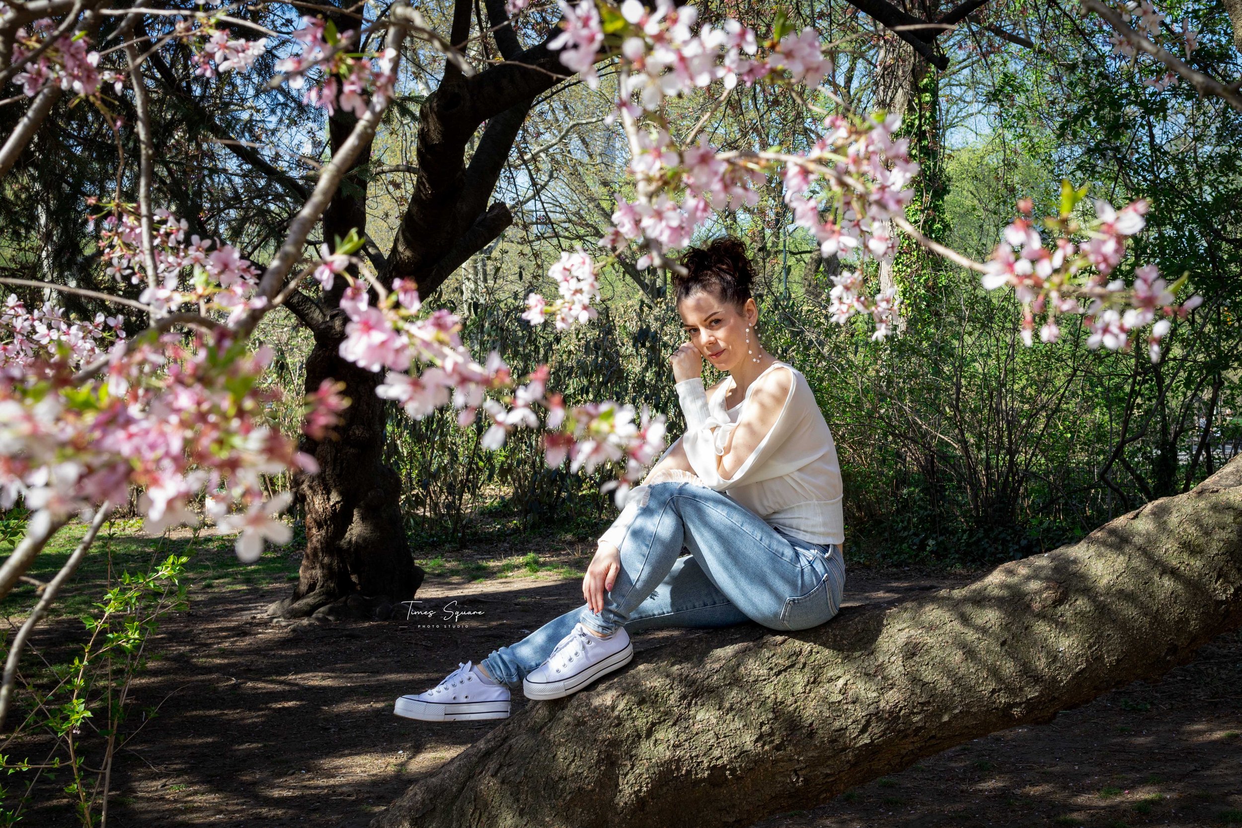 A woman enjoying a spring photoshoot under blooming cherry blossom trees in Central Park, New York City.
