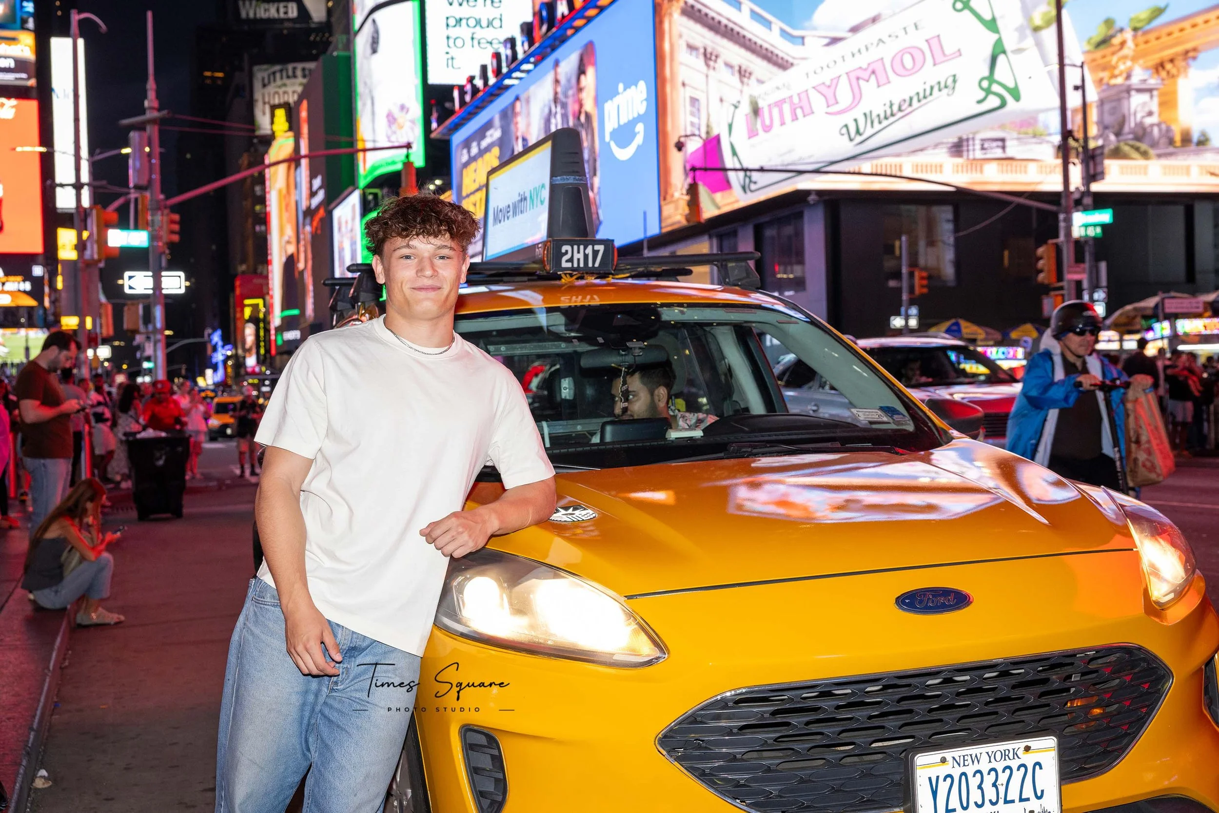 A man posing in front of a yellow cab in Times Square at night