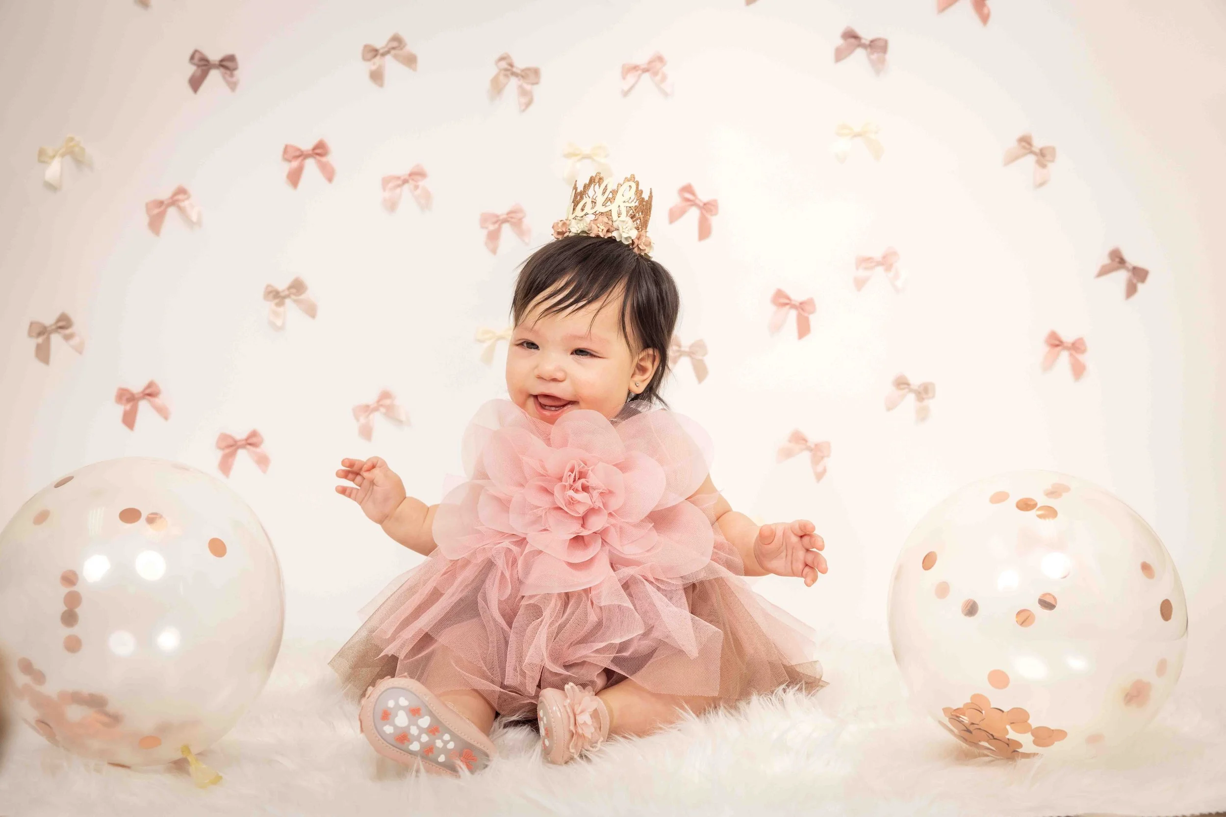 Baby in pink dress and crown surrounded by balloons