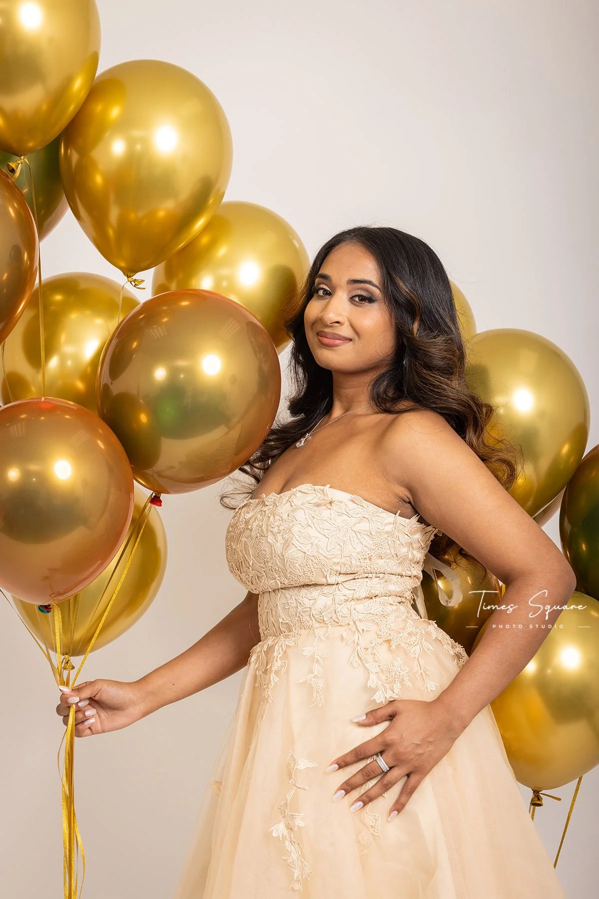 Elegant birthday studio portrait featuring a model in a champagne-colored dress surrounded by golden balloons during a custom birthday photoshoot at our New York City studio.