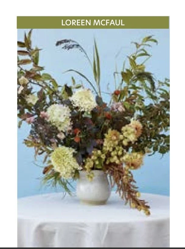 Floral arrangement in a vase on table with text "LOREEN MCFAUL" at top, against light blue background.