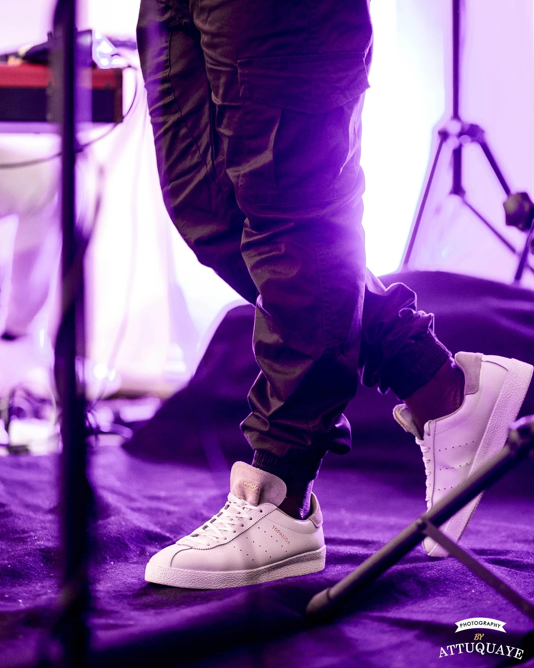 Person wearing white sneakers and dark cargo pants on stage with purple lighting.