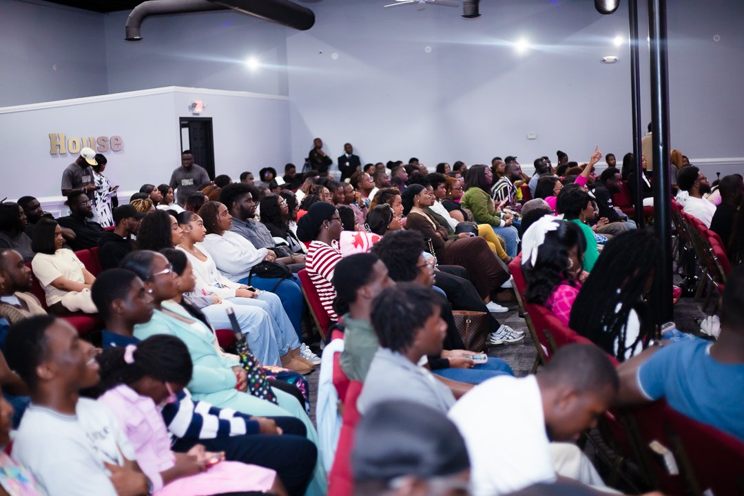 A diverse audience seated in rows at an indoor event, attentively listening.