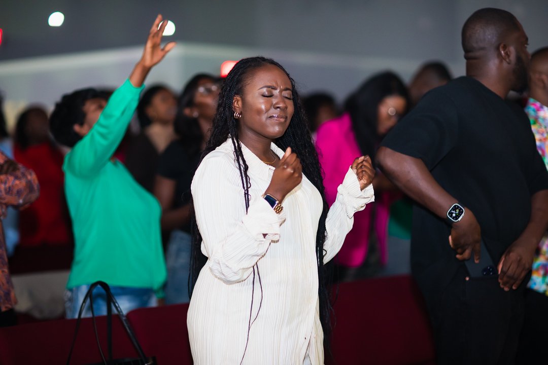 People worshiping with eyes closed and hands raised in a church setting.