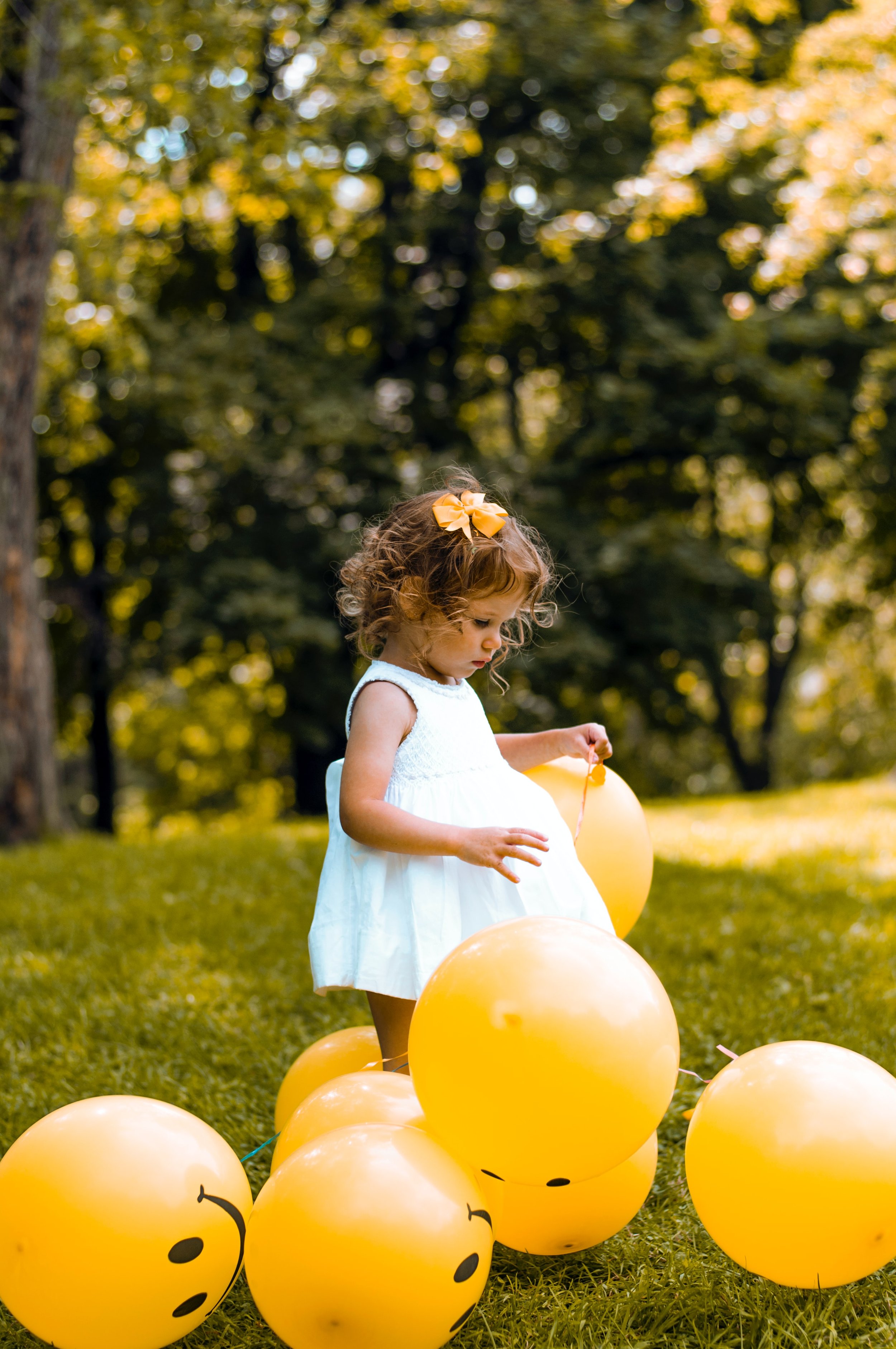Young child plays with yellow happy face balloons in fun speech and language therapy outside at home with therapist for NDIS