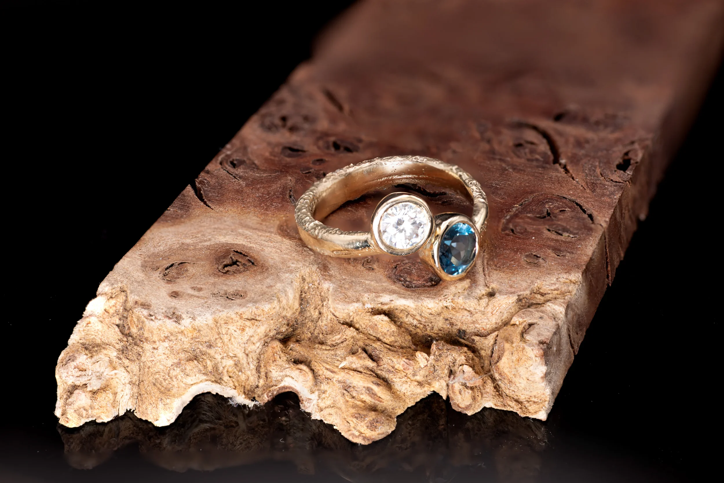 Close-up of a wooden surface with a gold ring featuring a diamond and a London Blue topaz on it.