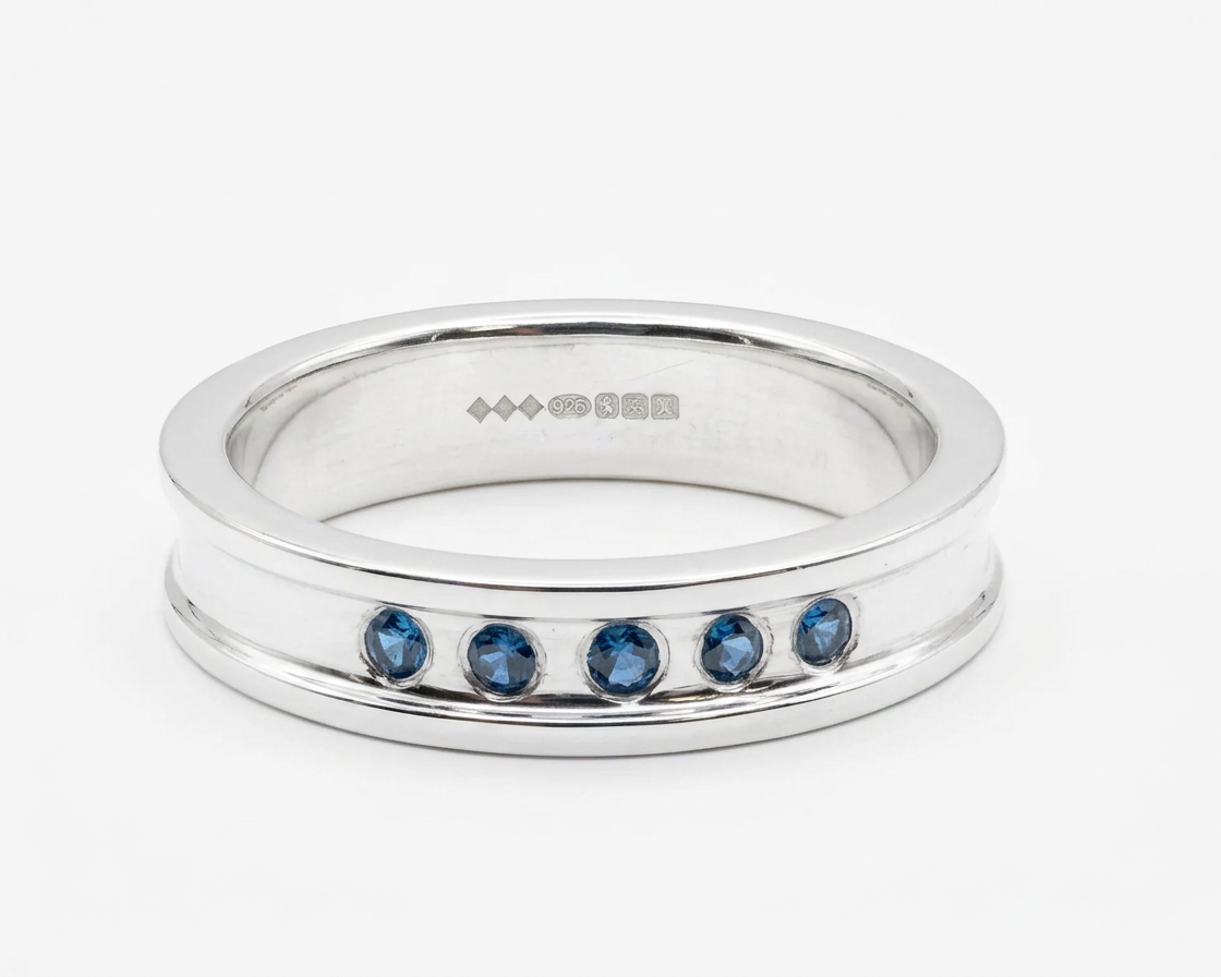 Silver ring with five blue gemstones embedded in the band, photographed against a white background.