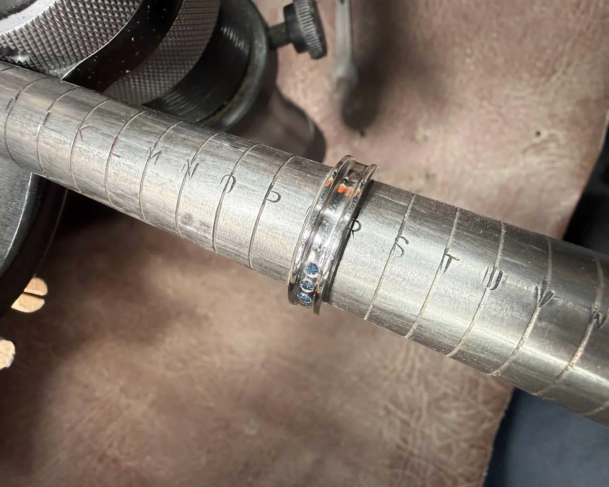 Close-up of a metal shaft with a ring and markings, placed on a textured surface.
