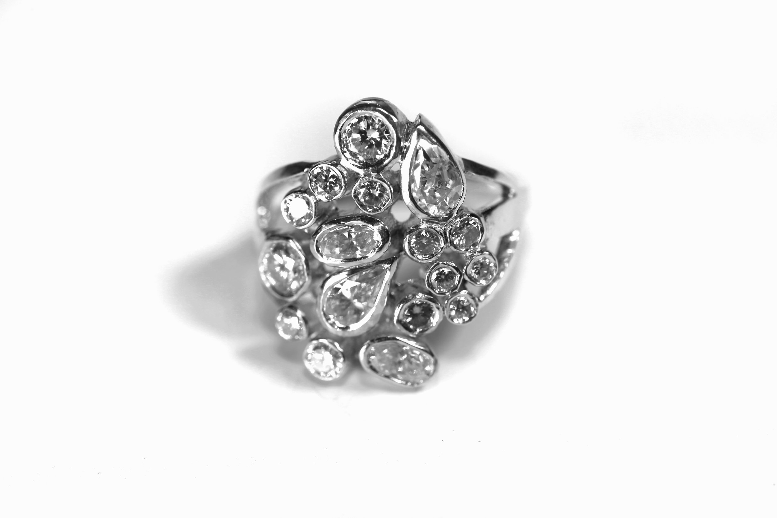 Close-up black and white photo of a silver ring adorned with multiple small and large gemstones arranged in a floral pattern.