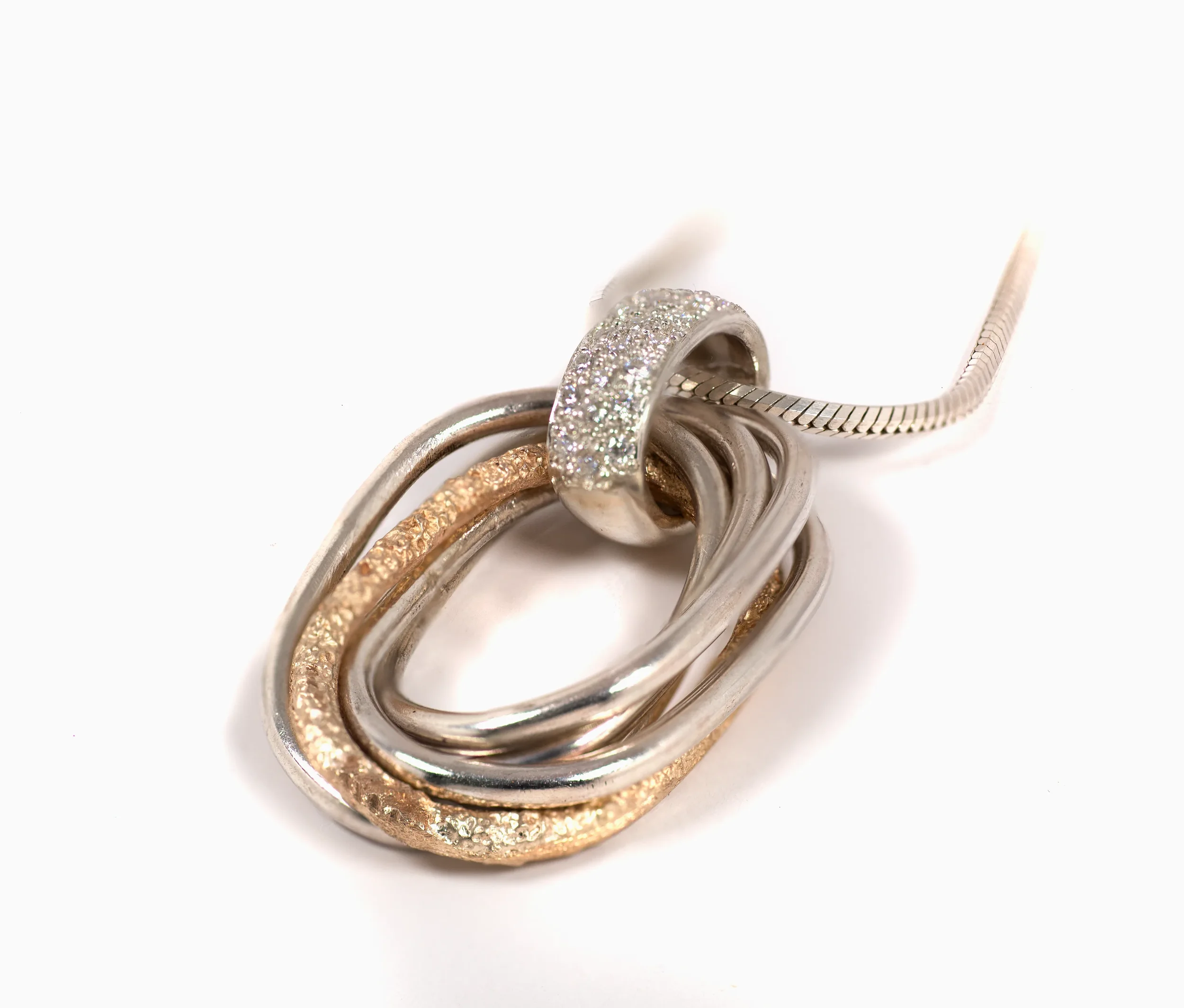 Multiple intertwined silver, gold, and diamond-studded rings with a silver necklace on a white background.