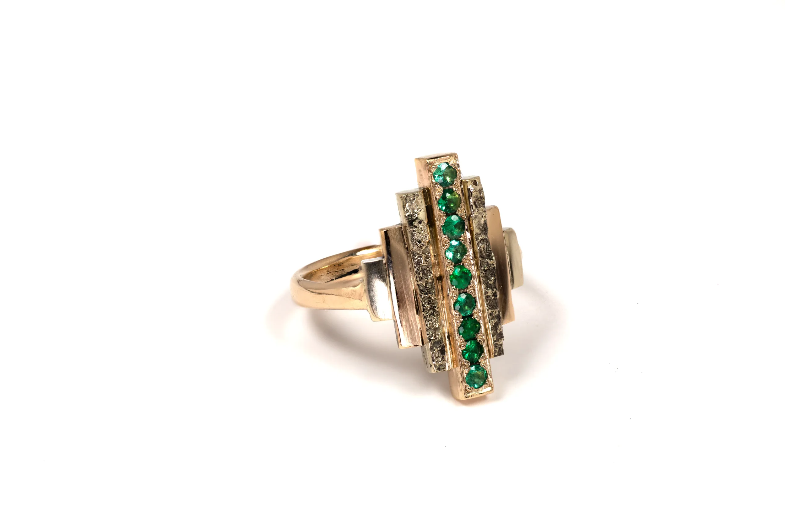 Close-up of a Sculpted Horizon ring showing the contrast between raw sand texture and high-polish Art Deco edges, set with Brazilian Emeralds.