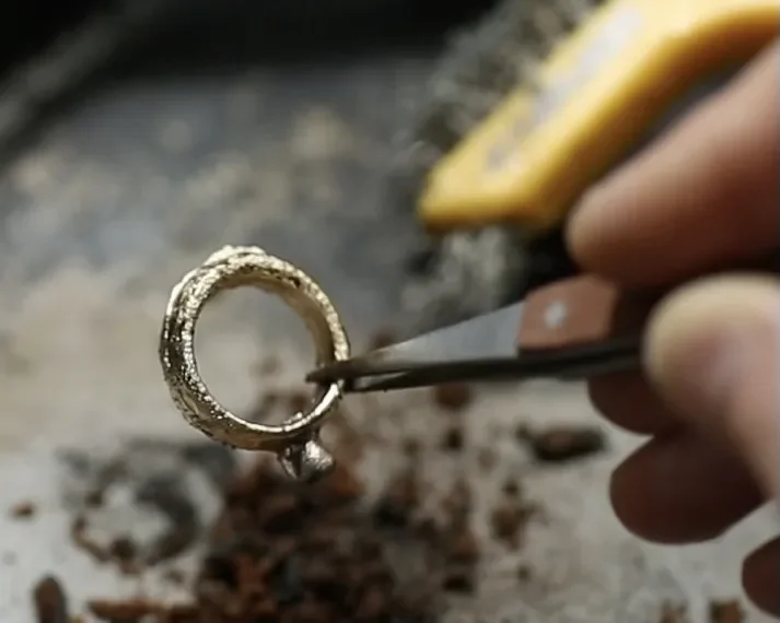 A person holding a jewelry ring with pliers in one hand and a tool in the other, working on the ring.