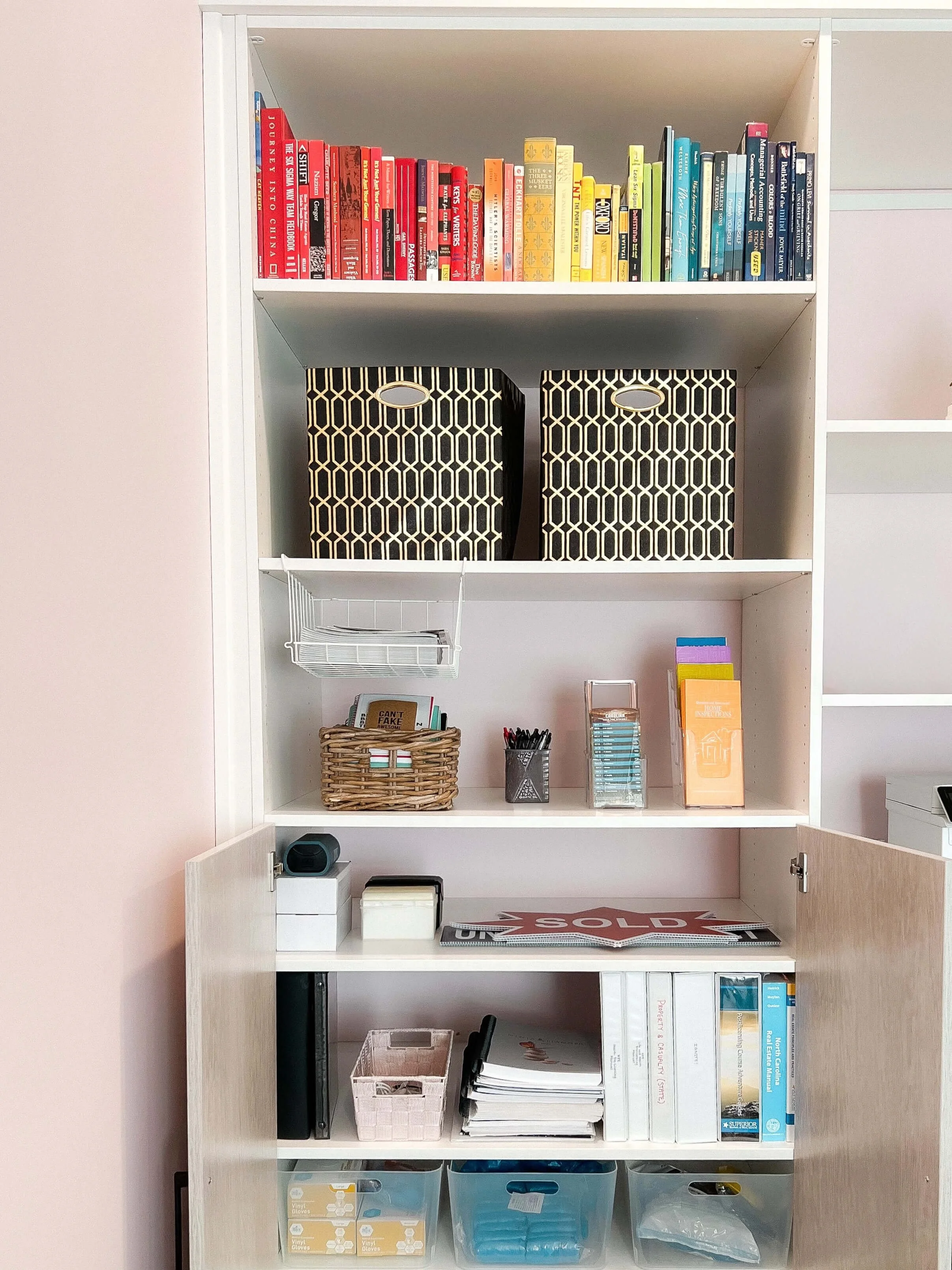 Organized home office for a Charlotte real estate professional, with color-coded books, patterned storage bins, labeled binders, and sorted supplies on white built-in shelving.