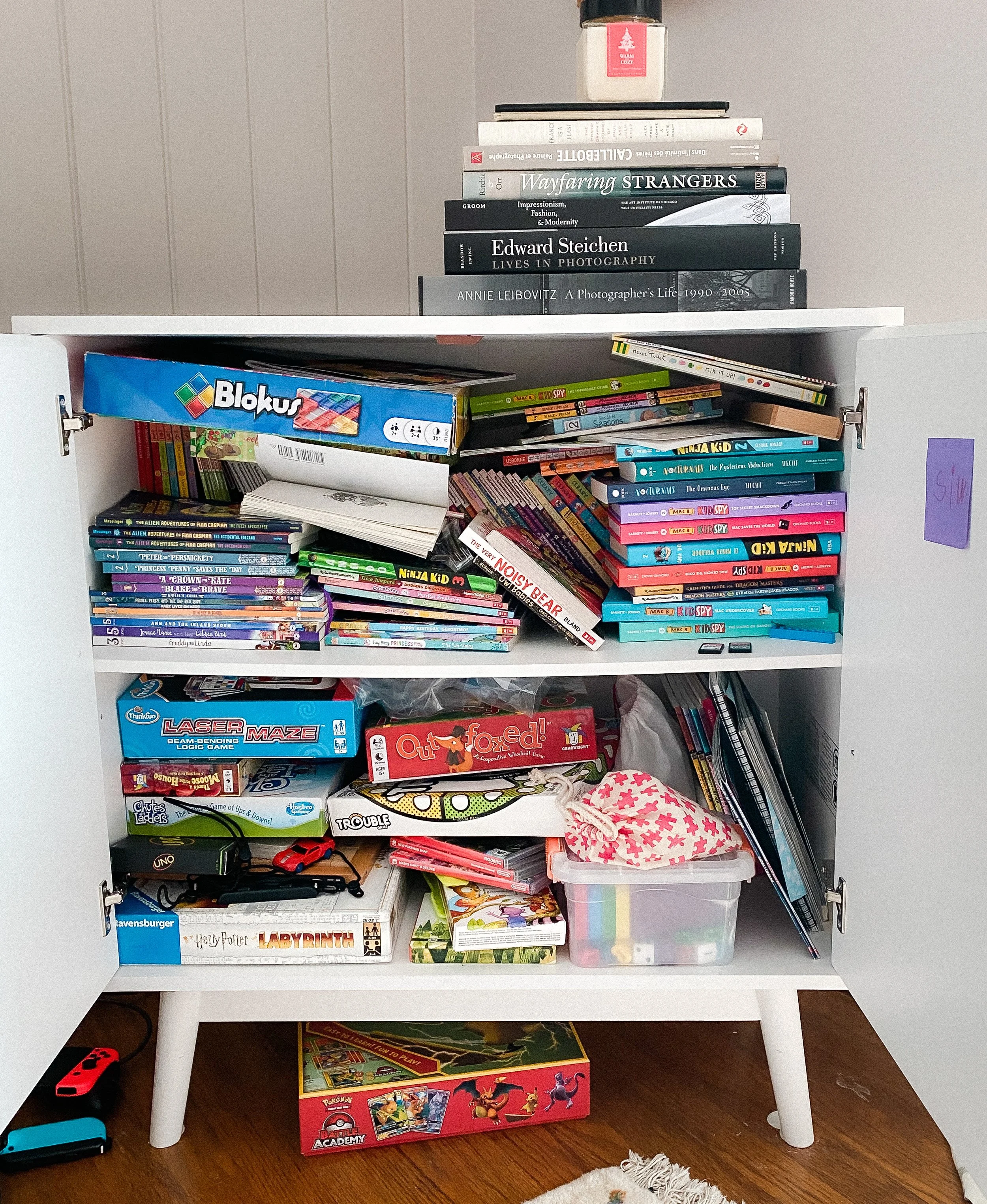 Before: Games and items piled up in a cluttered cabinet
