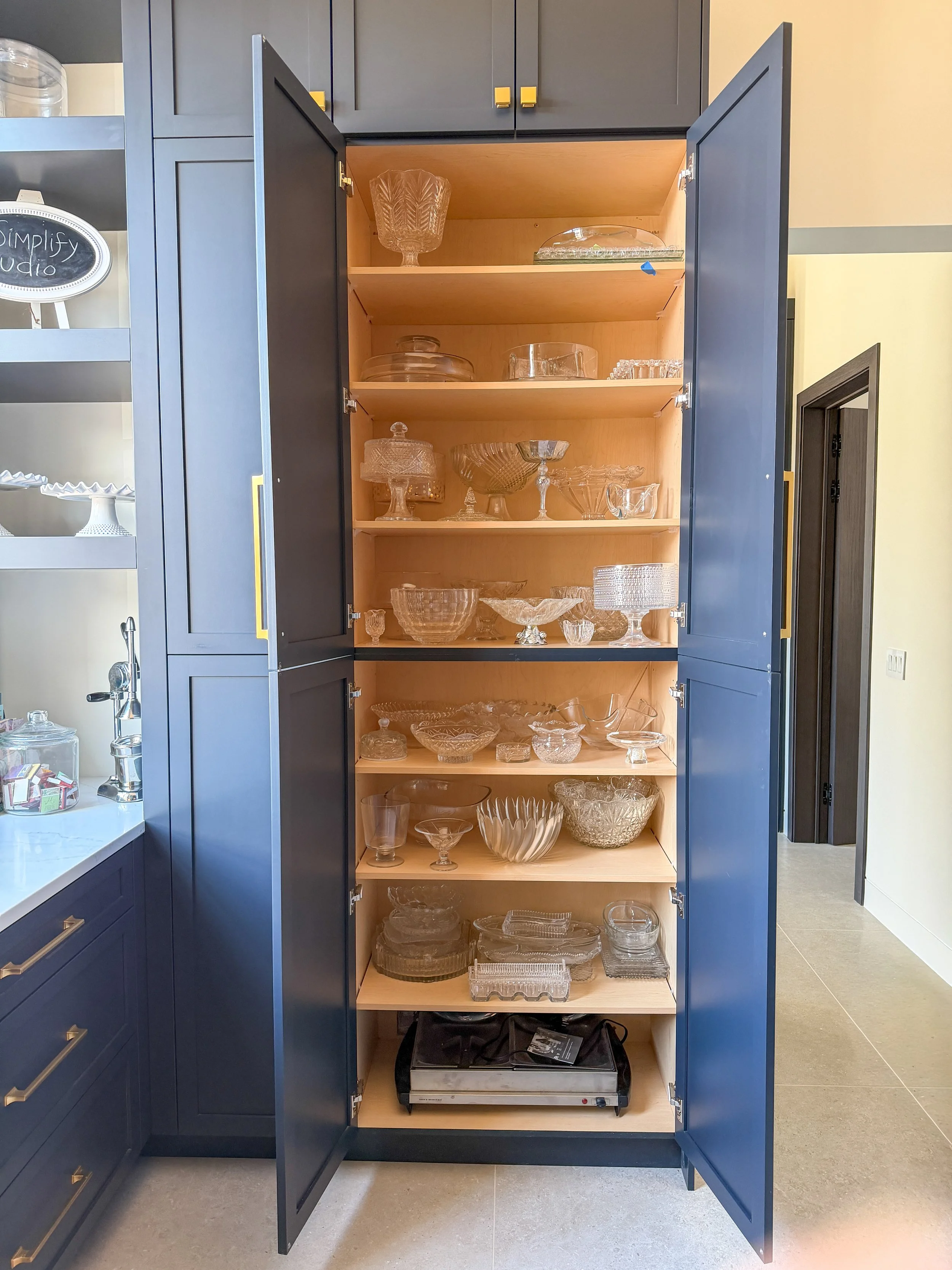 Kitchen cabinet with glass serving bowls, cake stands, and entertaining pieces neatly organized.