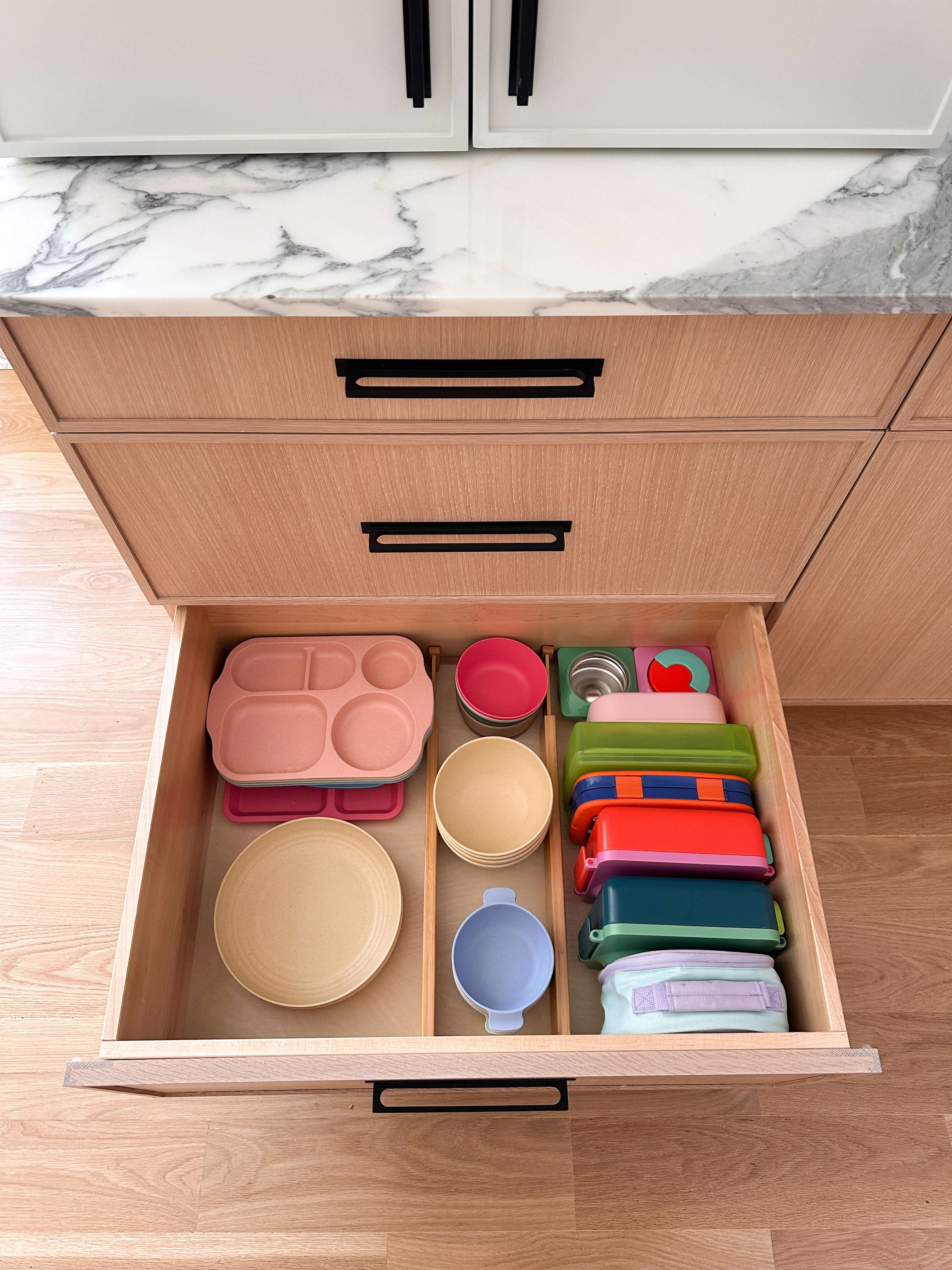 Organized kitchen drawer with children's lunch containers, bowls, plates, and food storage organized by category.