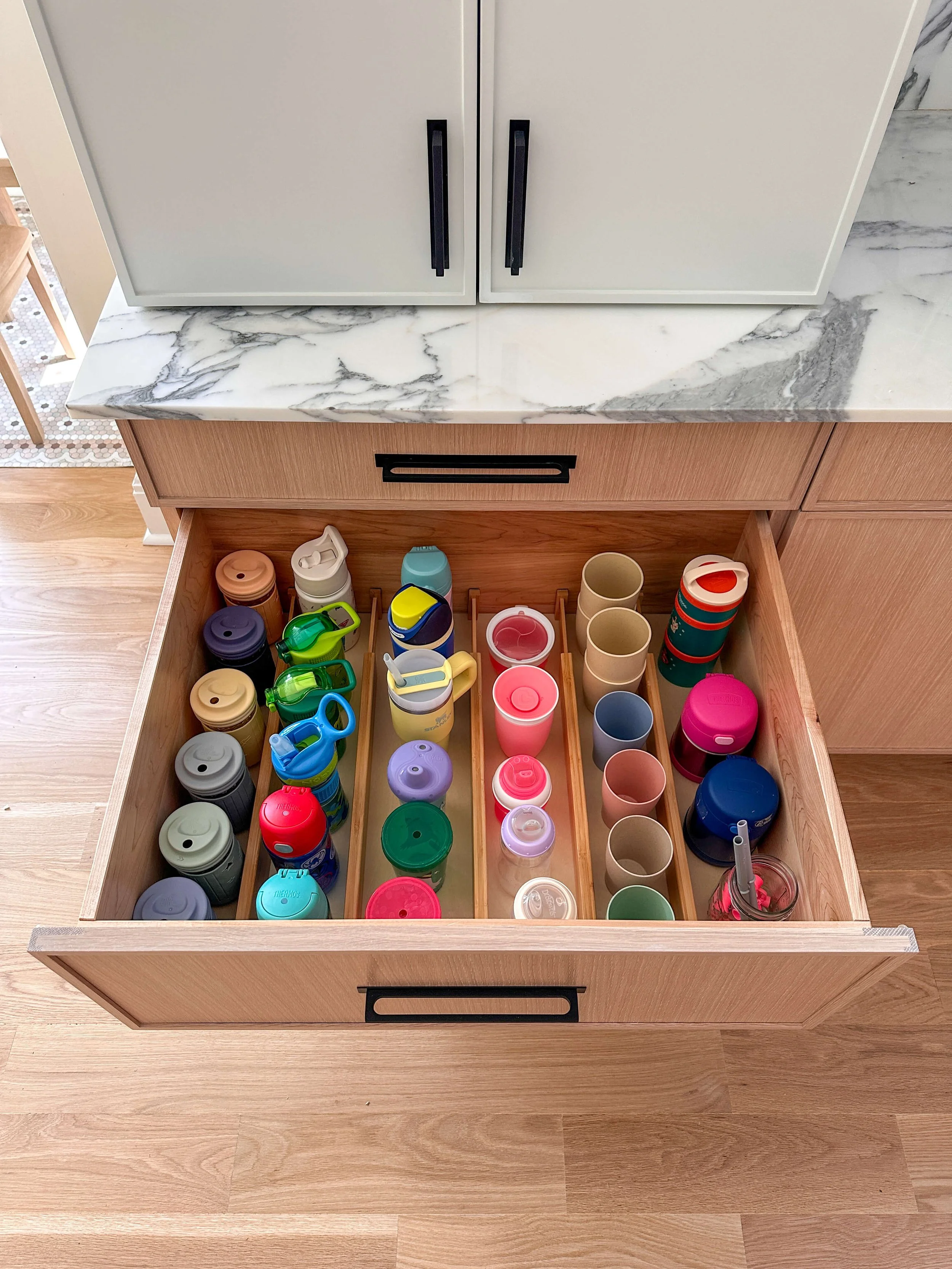 Kitchen drawer organized with reusable children's water bottles stored upright in divided compartments.