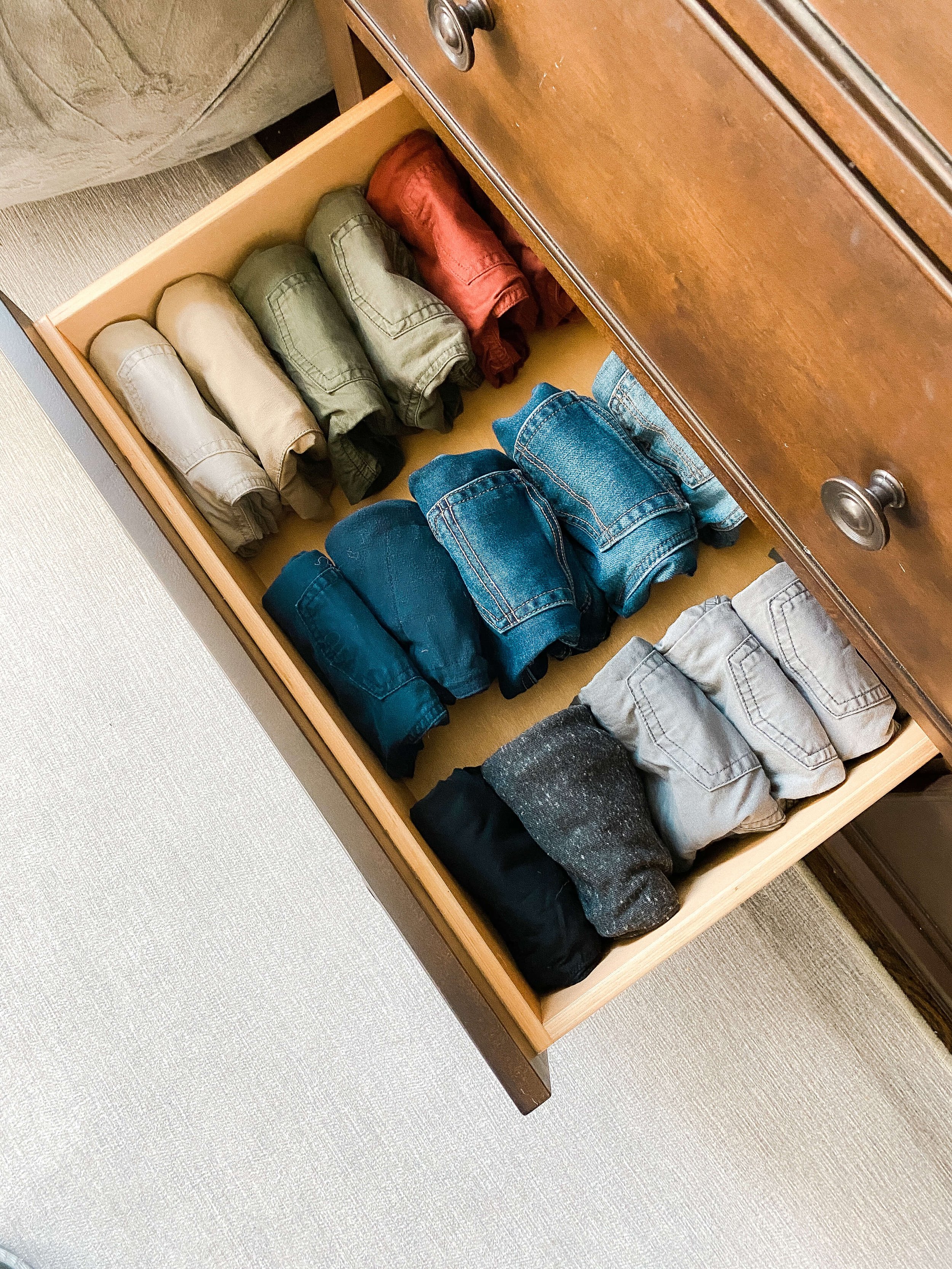 Children's clothing neatly folded and organized by category inside a dresser drawer.