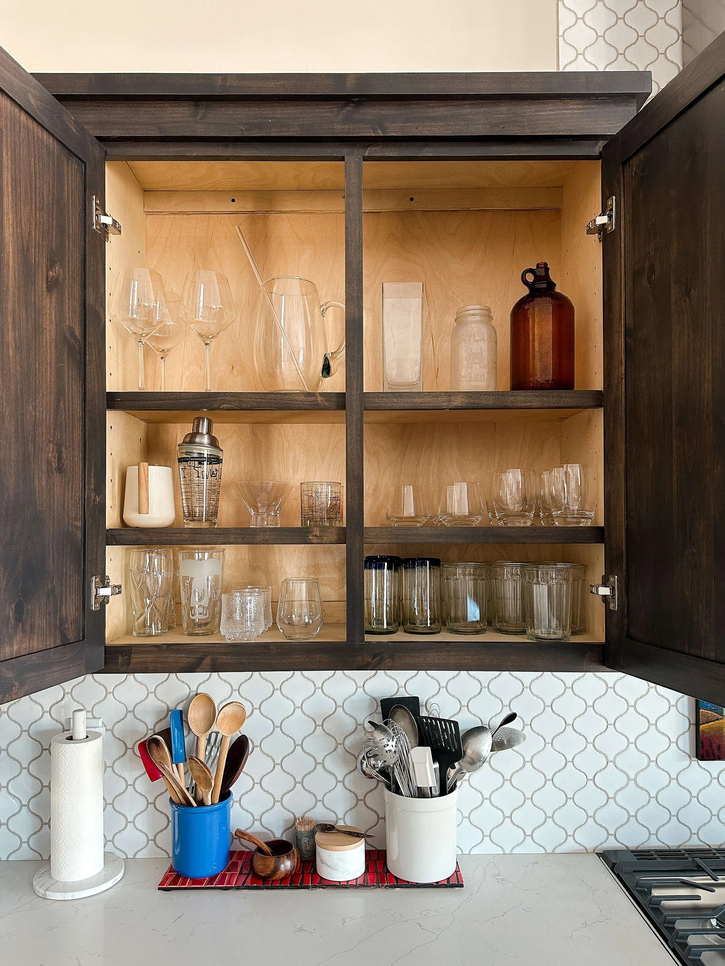 Kitchen cabinet with neatly organized glassware, cocktail tools, and drinkware.