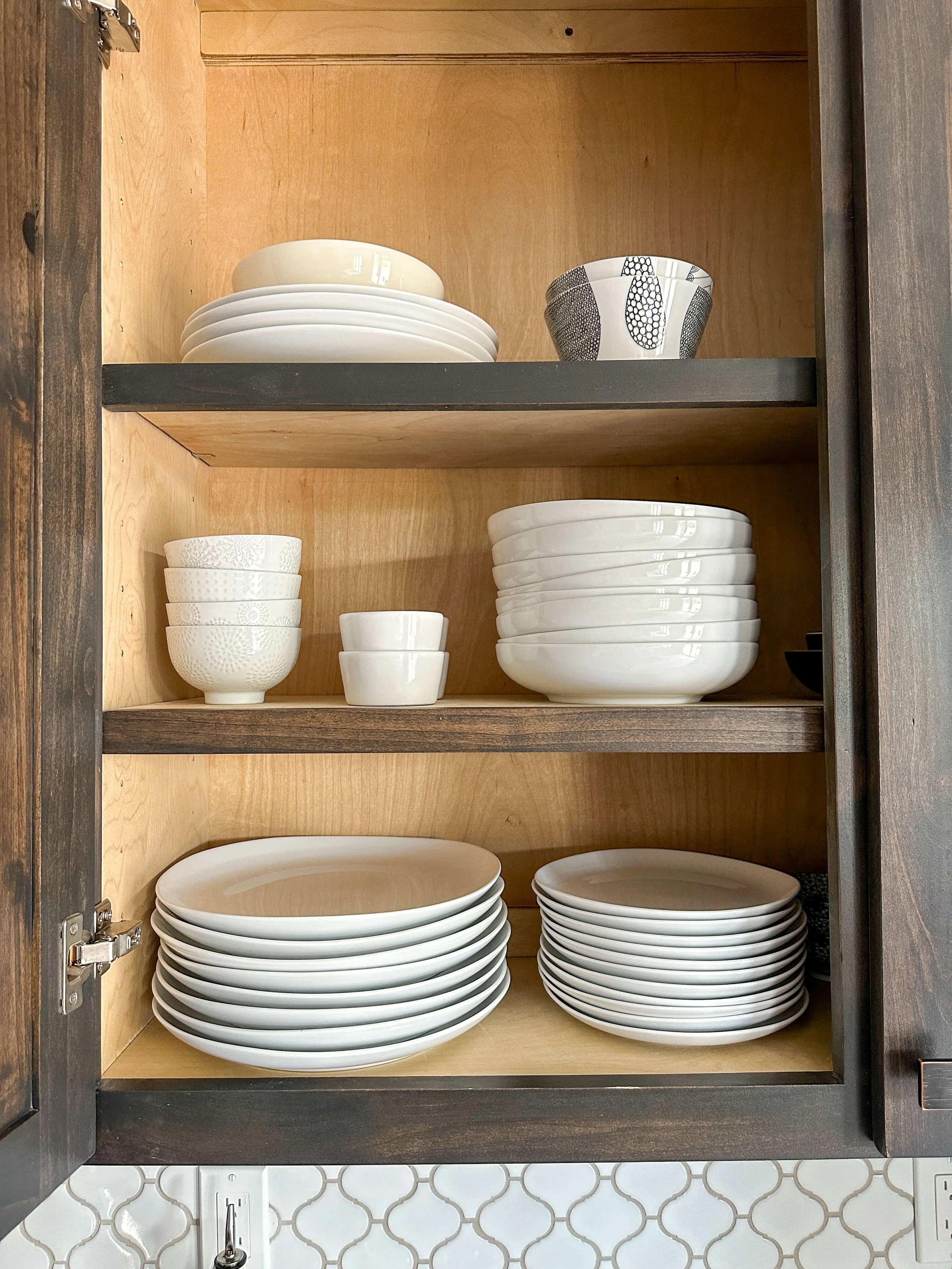 Kitchen cabinet with neatly stacked dinner plates, bowls, and serving dishes.