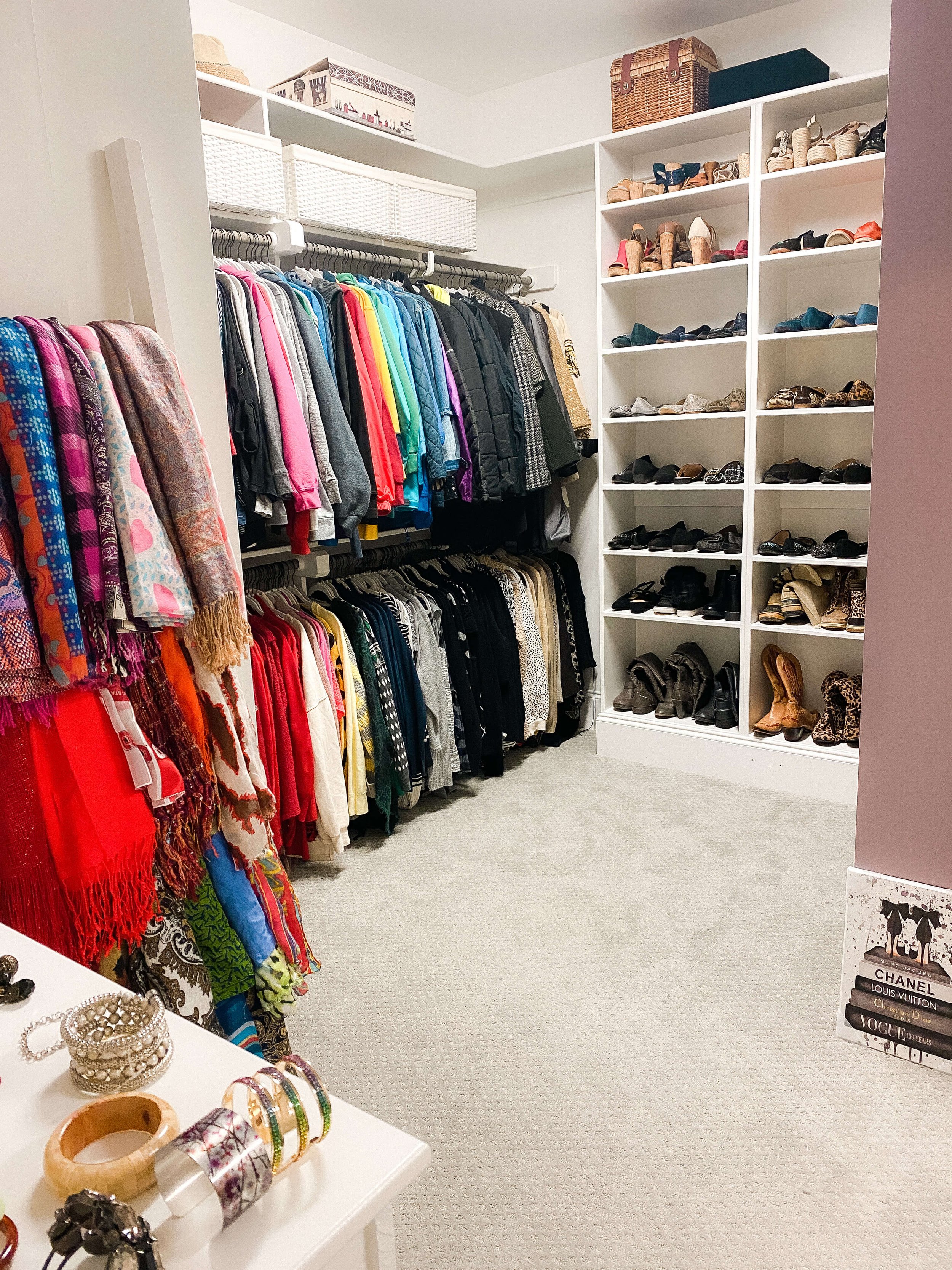 Organized walk-in closet with folded accessories, hanging clothing, and neatly arranged shoe shelves