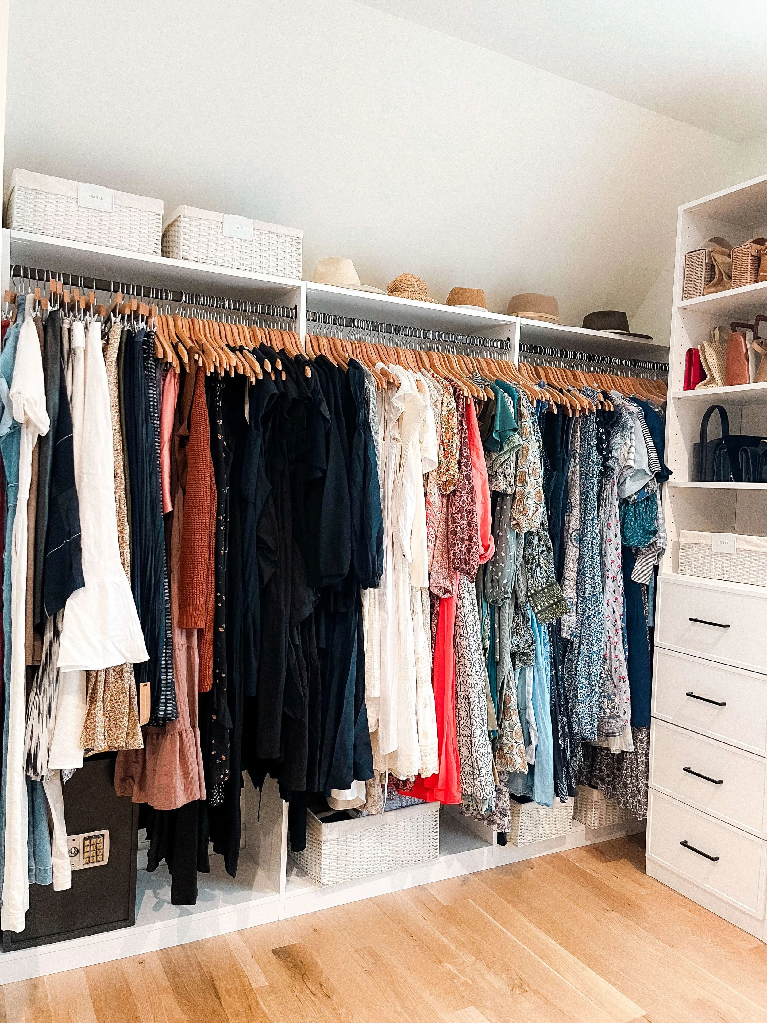 Organized primary closet with hanging clothing, labeled storage bins, handbags, and drawers