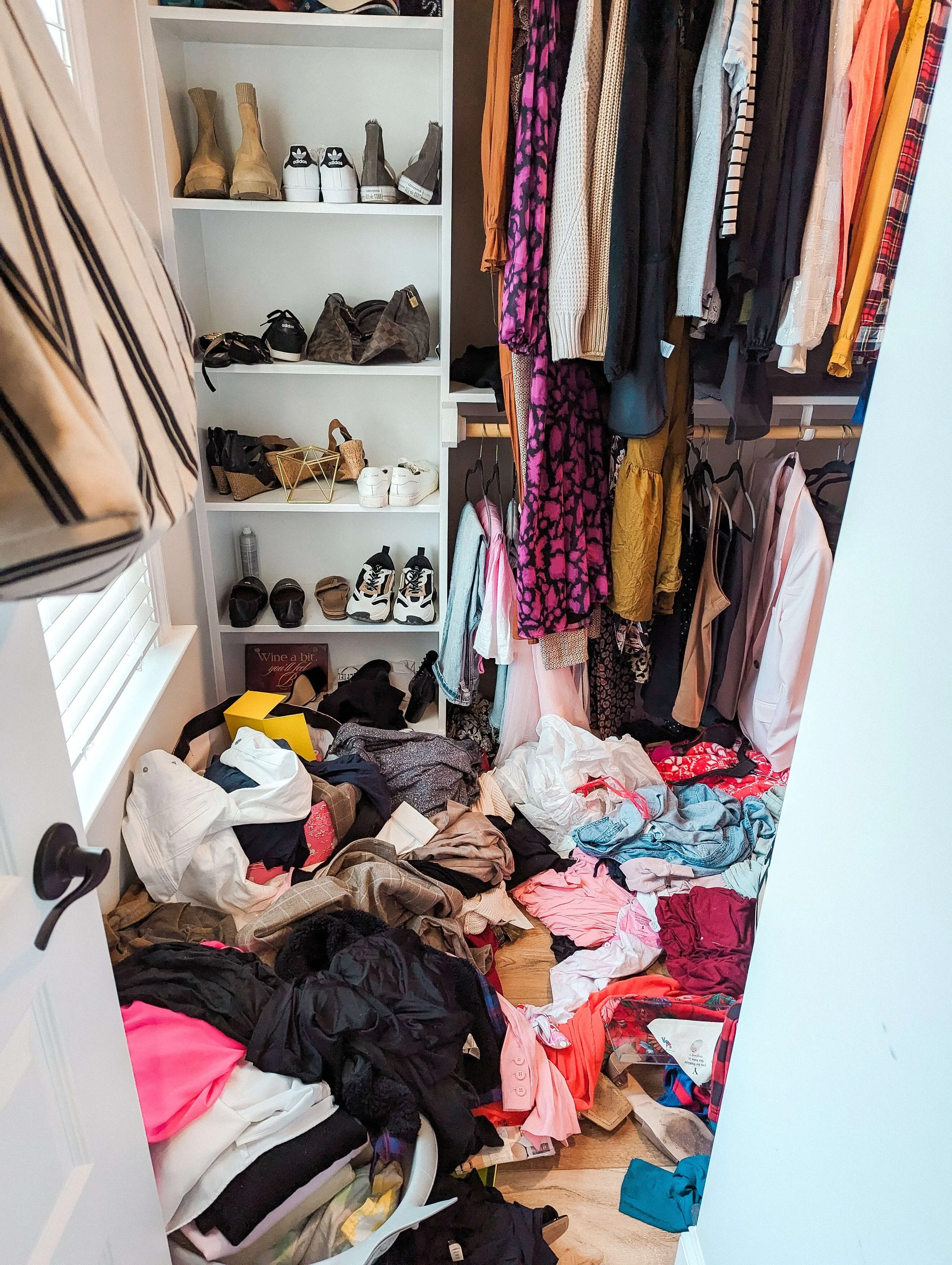 Cluttered primary closet before organizing with clothing and accessories covering the floor.