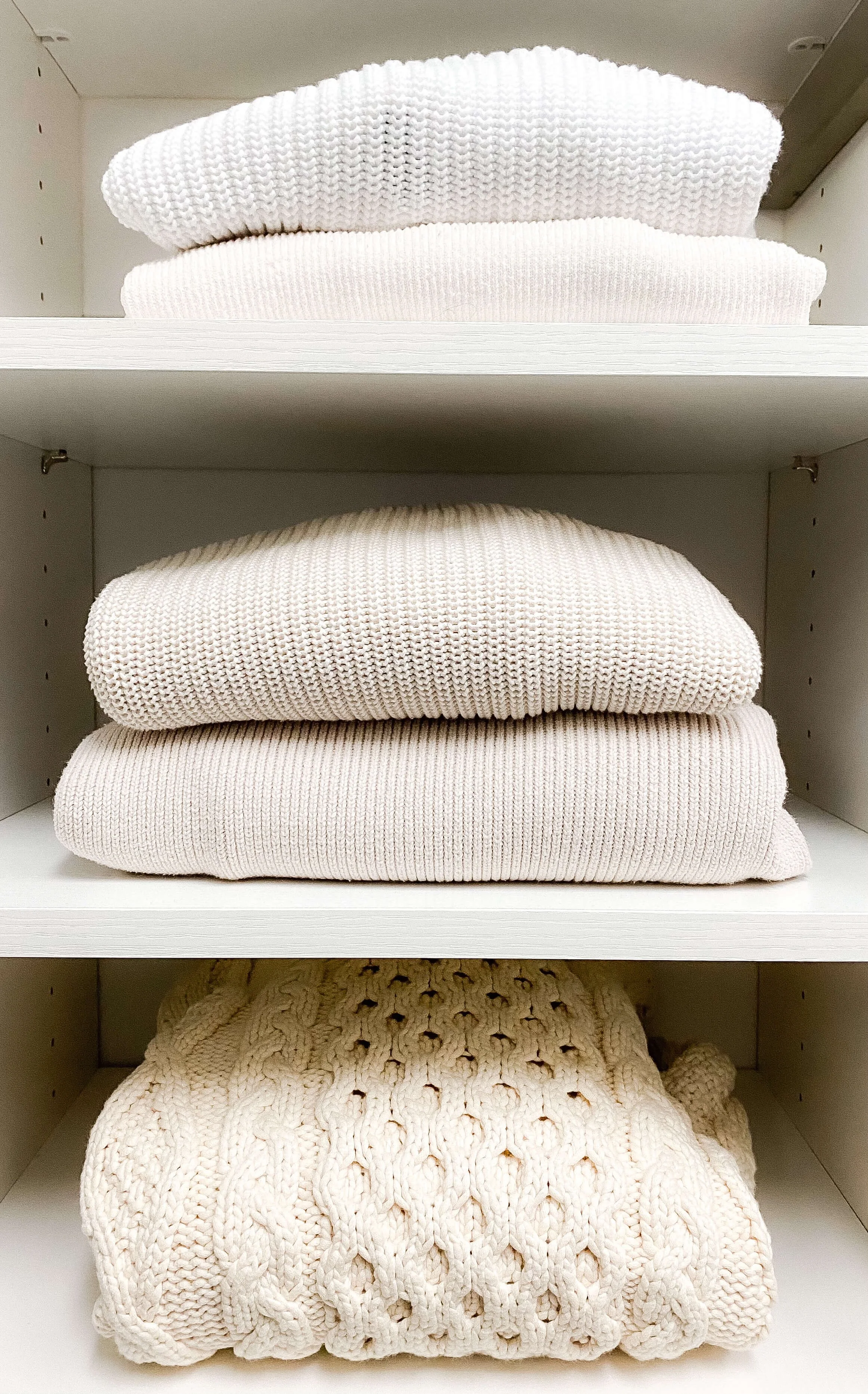 Folded sweaters neatly stacked on white closet shelves.