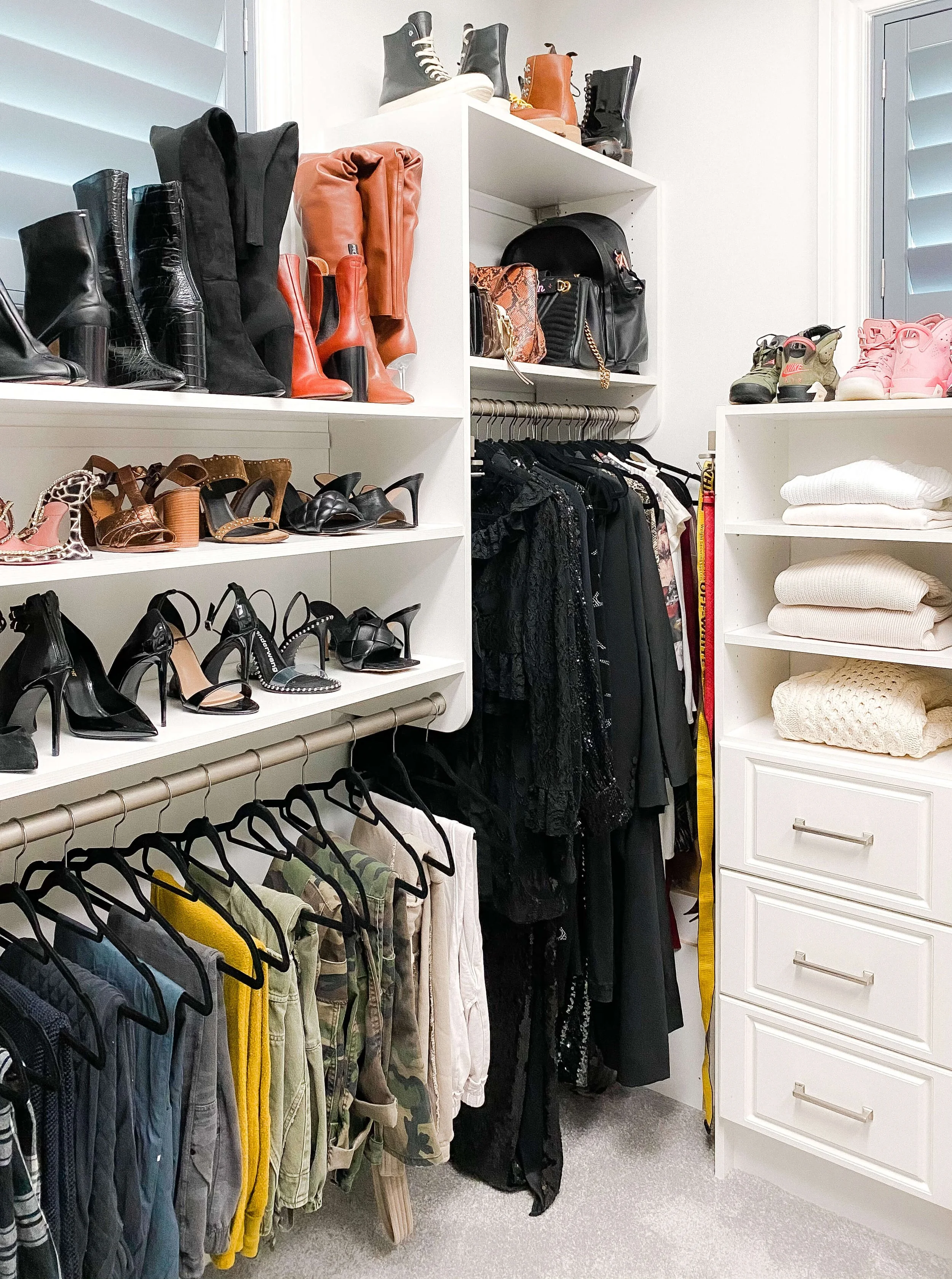 Organized primary closet with custom shelving, hanging clothes, boots, handbags, and folded sweaters.