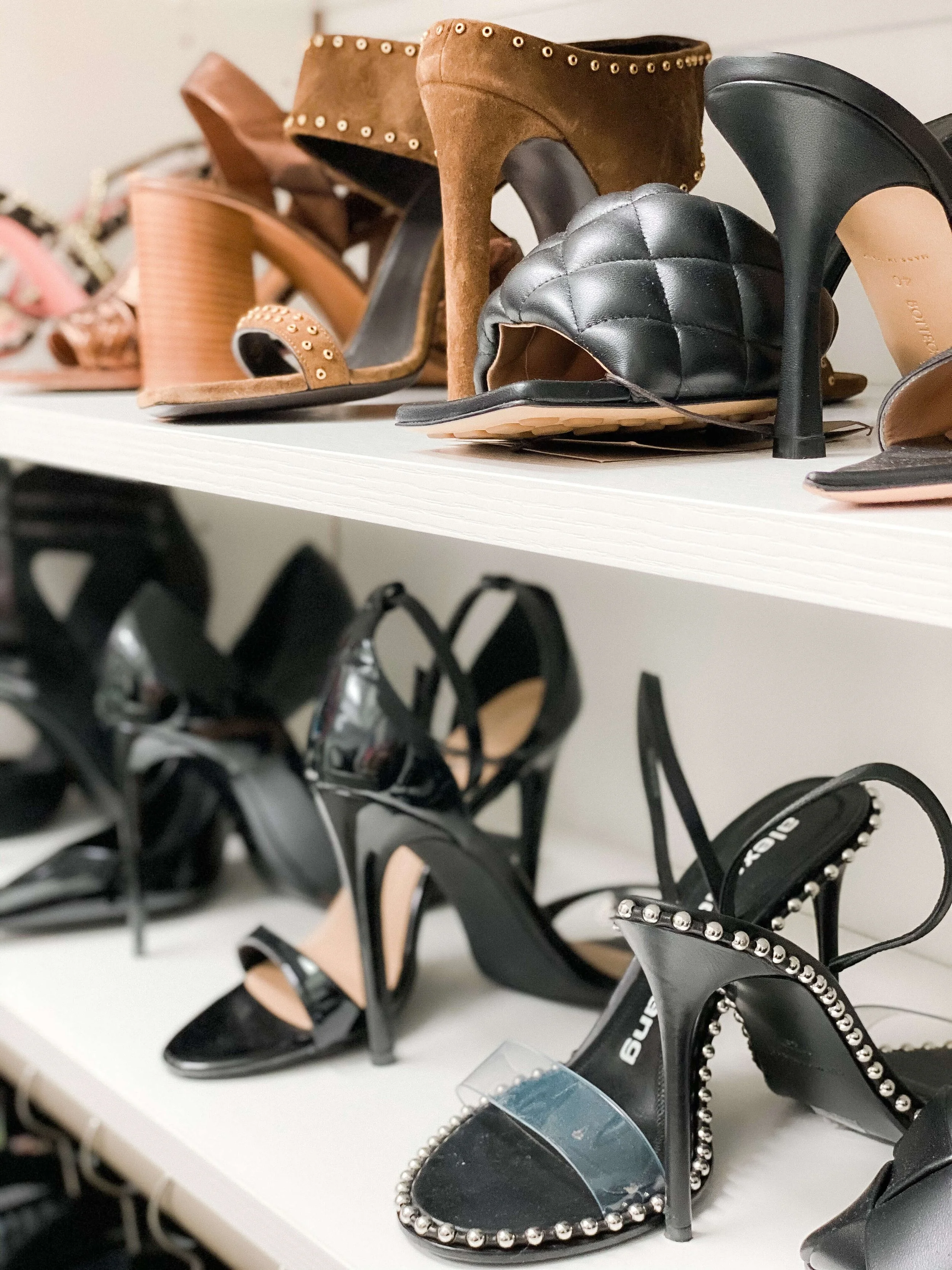 Designer shoes neatly arranged on white closet shelves.