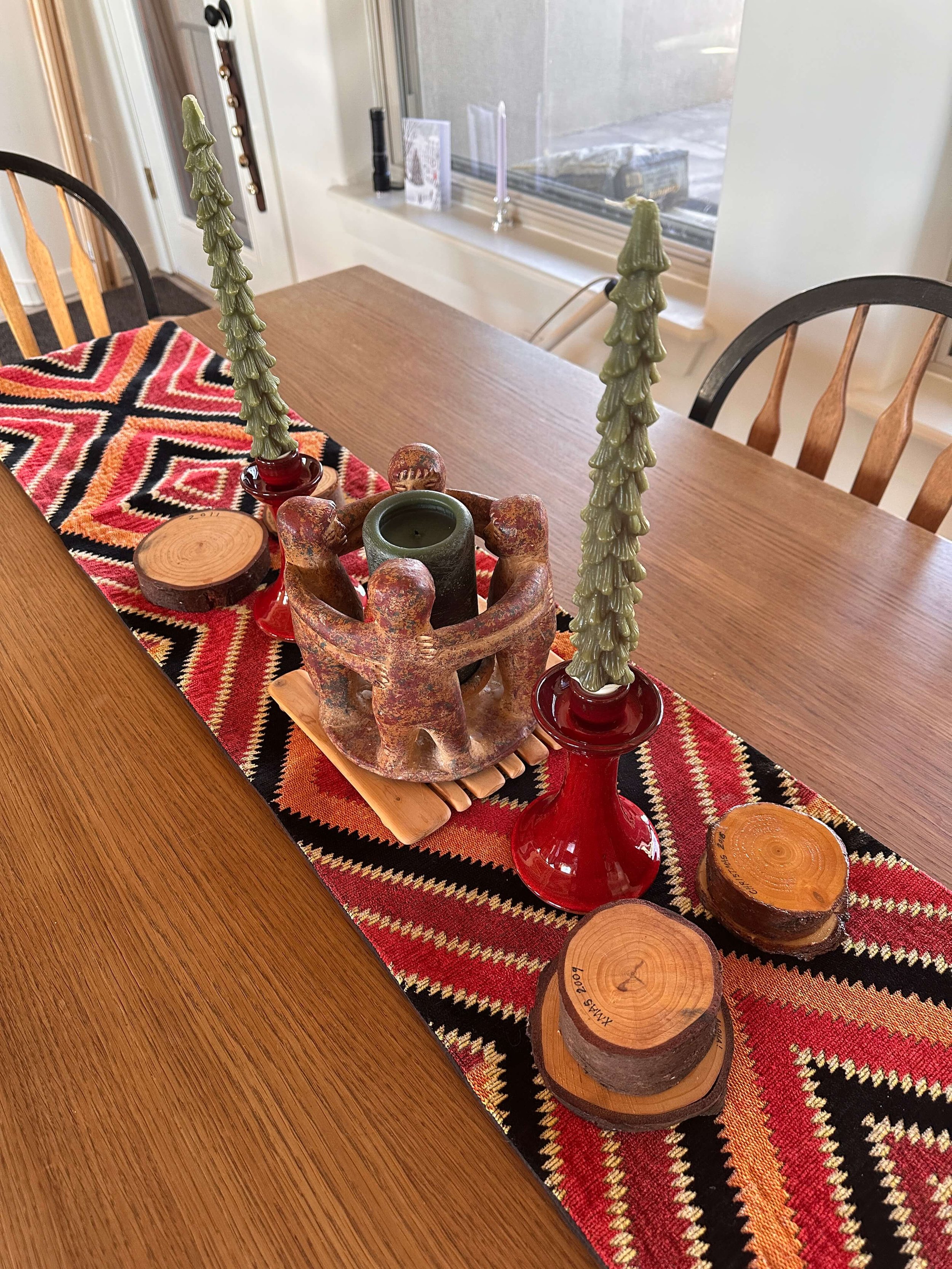  A holiday dining table with a woven runner, tree candles, and carved decor 