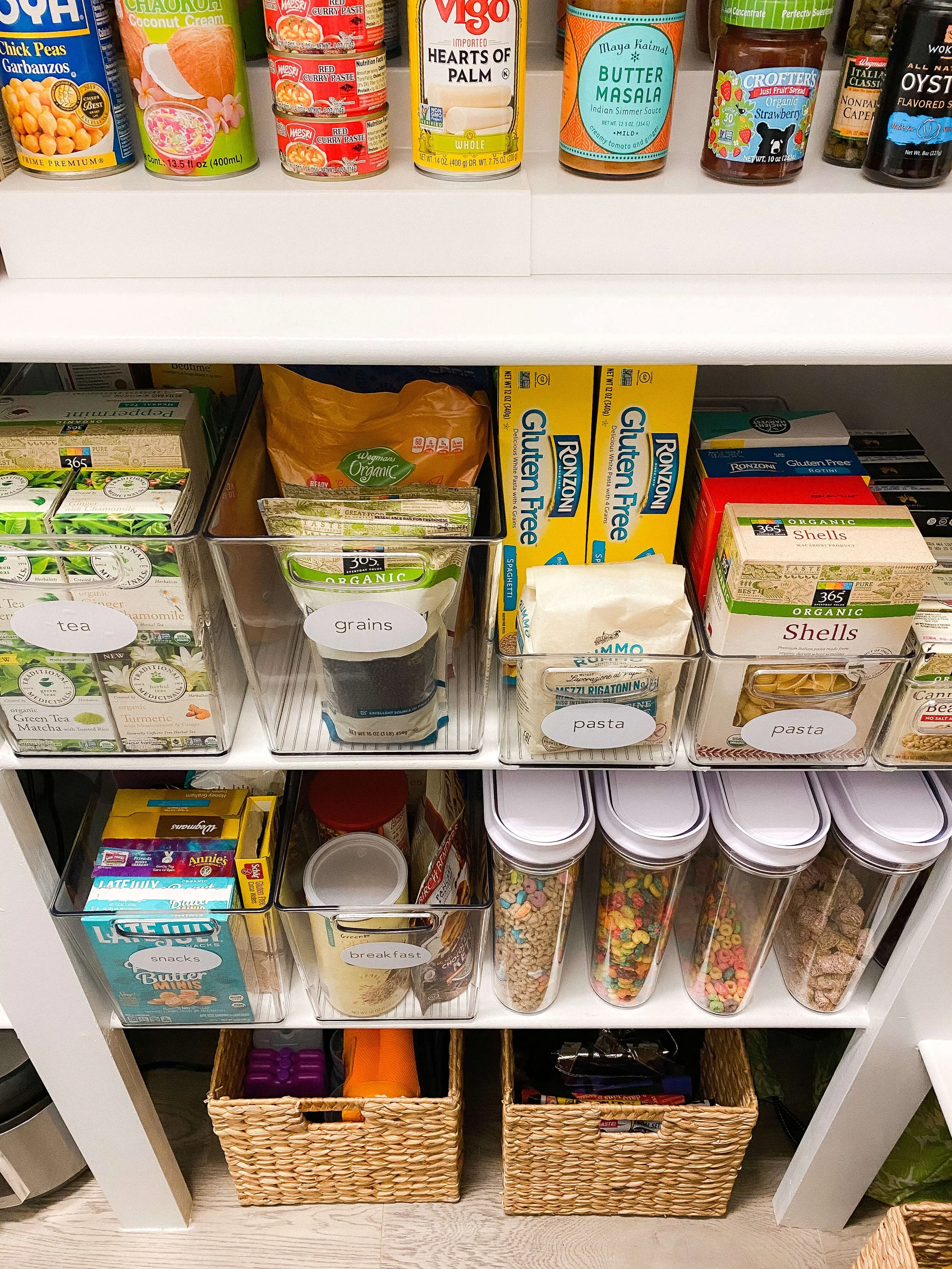  Clear labeled containers for tea, grains, and pasta beside cereal decanted into matching canisters 