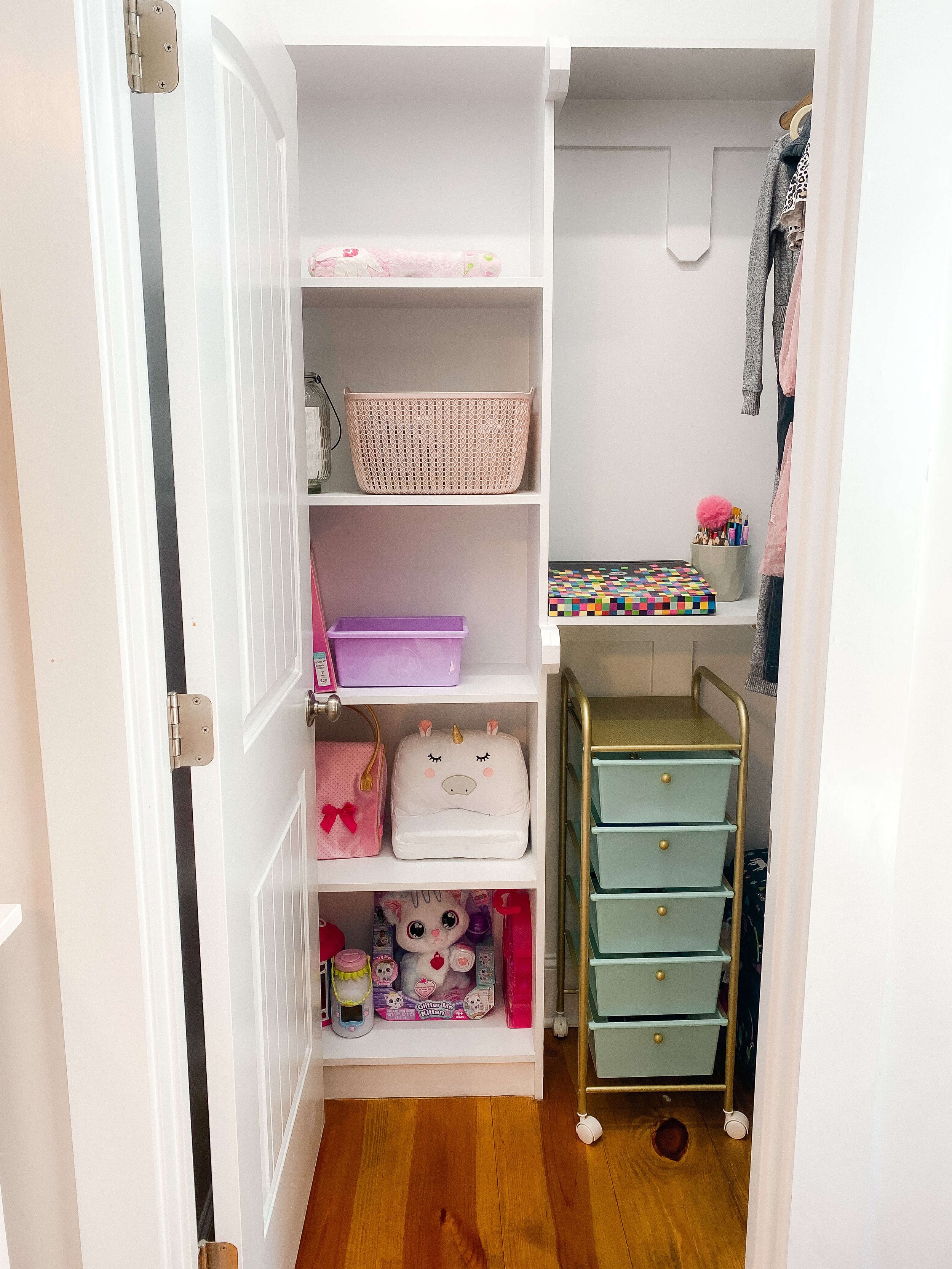  The same closet after organizing, with a rolling drawer cart, labeled bins on open shelves, a small homework nook with cups of pencils, and clothing on a low rod 