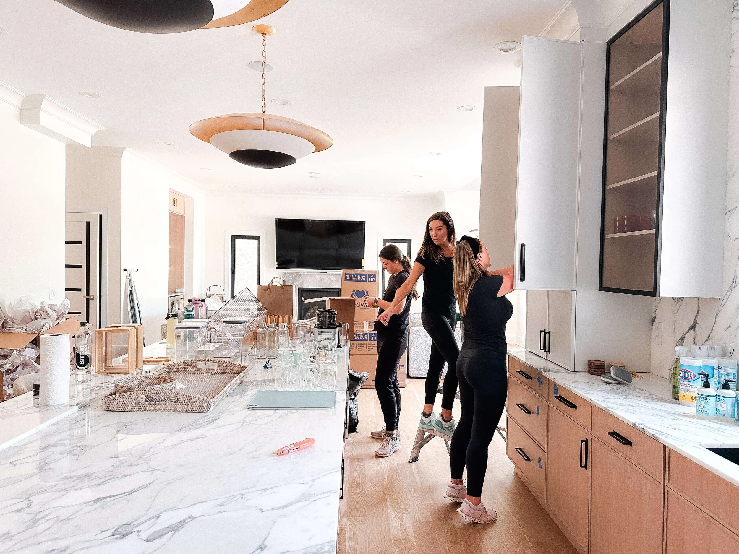 Professional organizers unpacking and arranging a kitchen with marble countertops, creating functional and visually calm spaces for a Raleigh home.