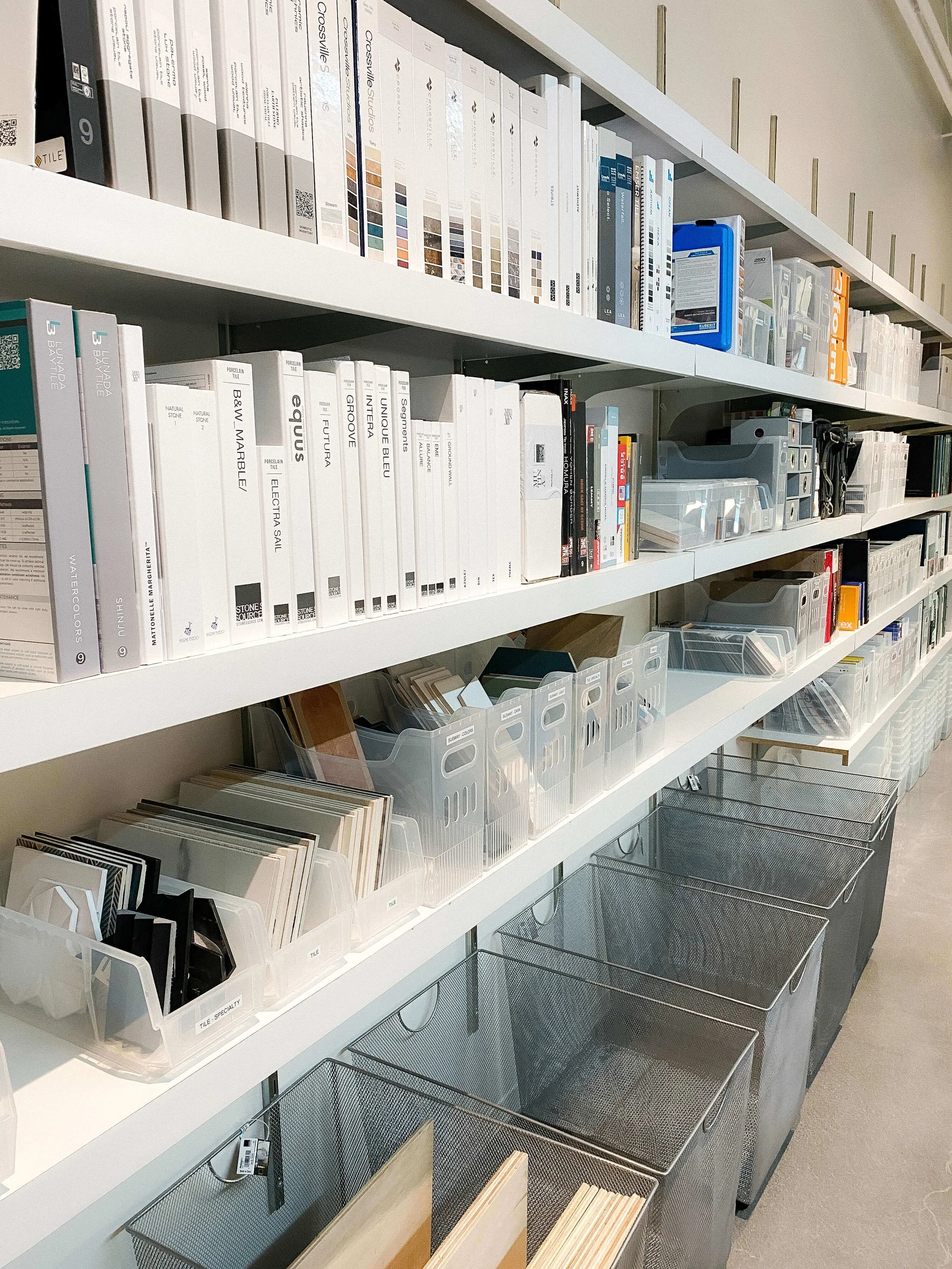 Architectural materials library organized with sample binders and tile samples in labeled bins on open shelving.