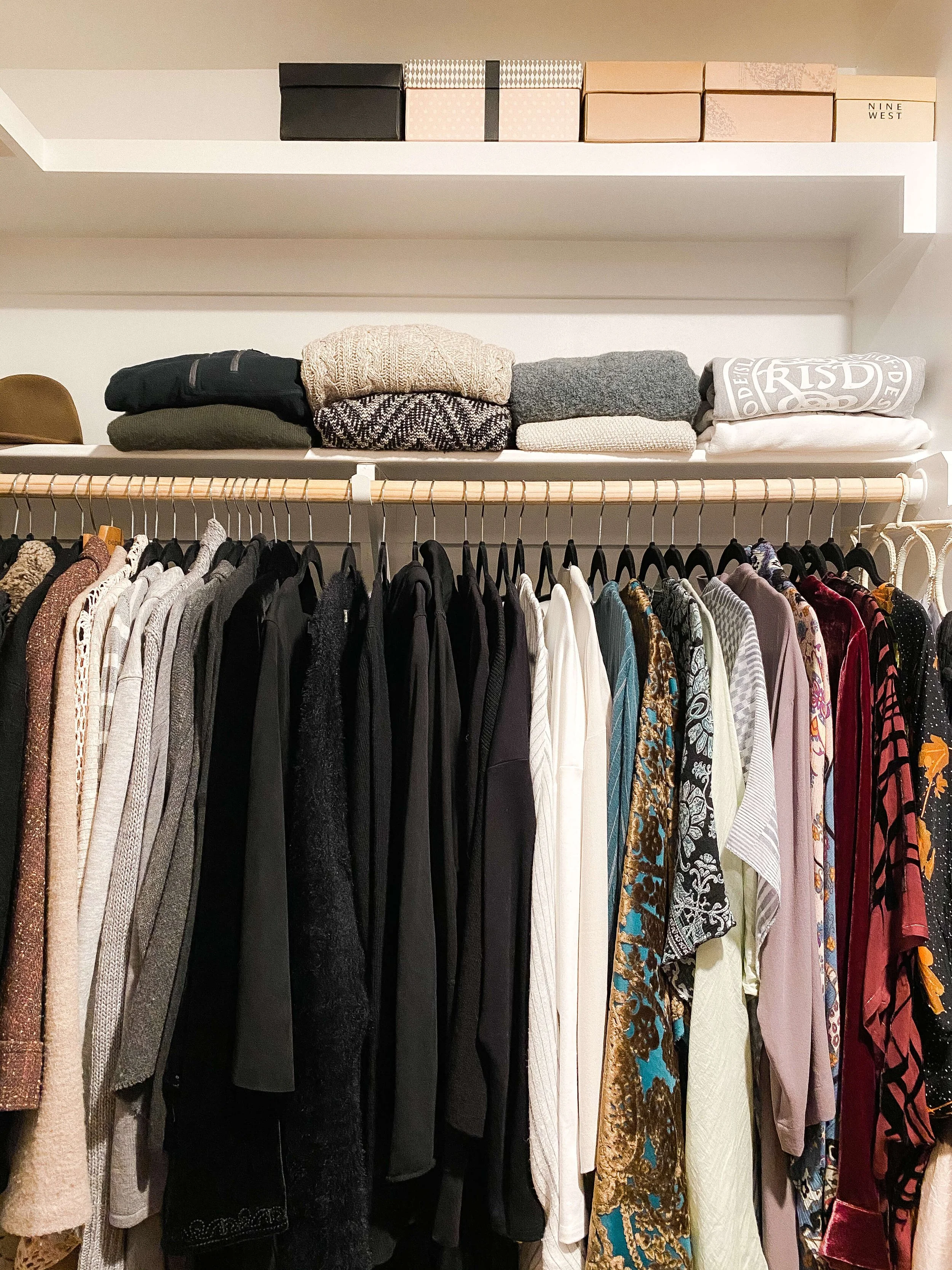Organized walk-in closet with summer clothing neatly hung by category, folded items stacked on shelves, and storage bins used for seasonal items and accessories
